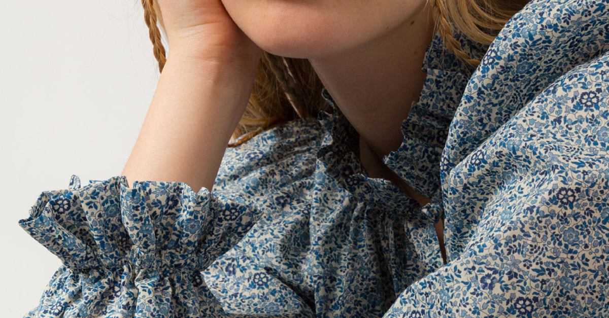 Woman in blue floral design shirt with frilled cuffs and neck and long puff sleeves