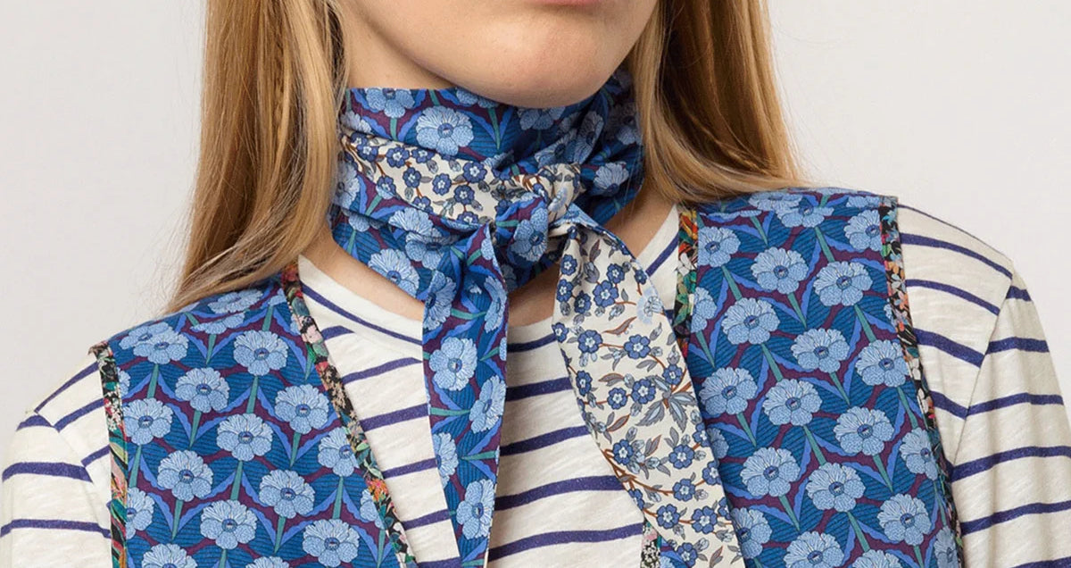 Woman with blue flower printed scarf around neck, blue and white striped t-shirt and blue flower patterned vest