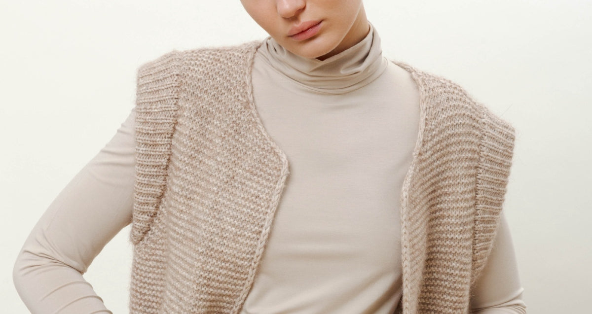 Woman in creme colored roll neck and knitted creme colored wool vest
