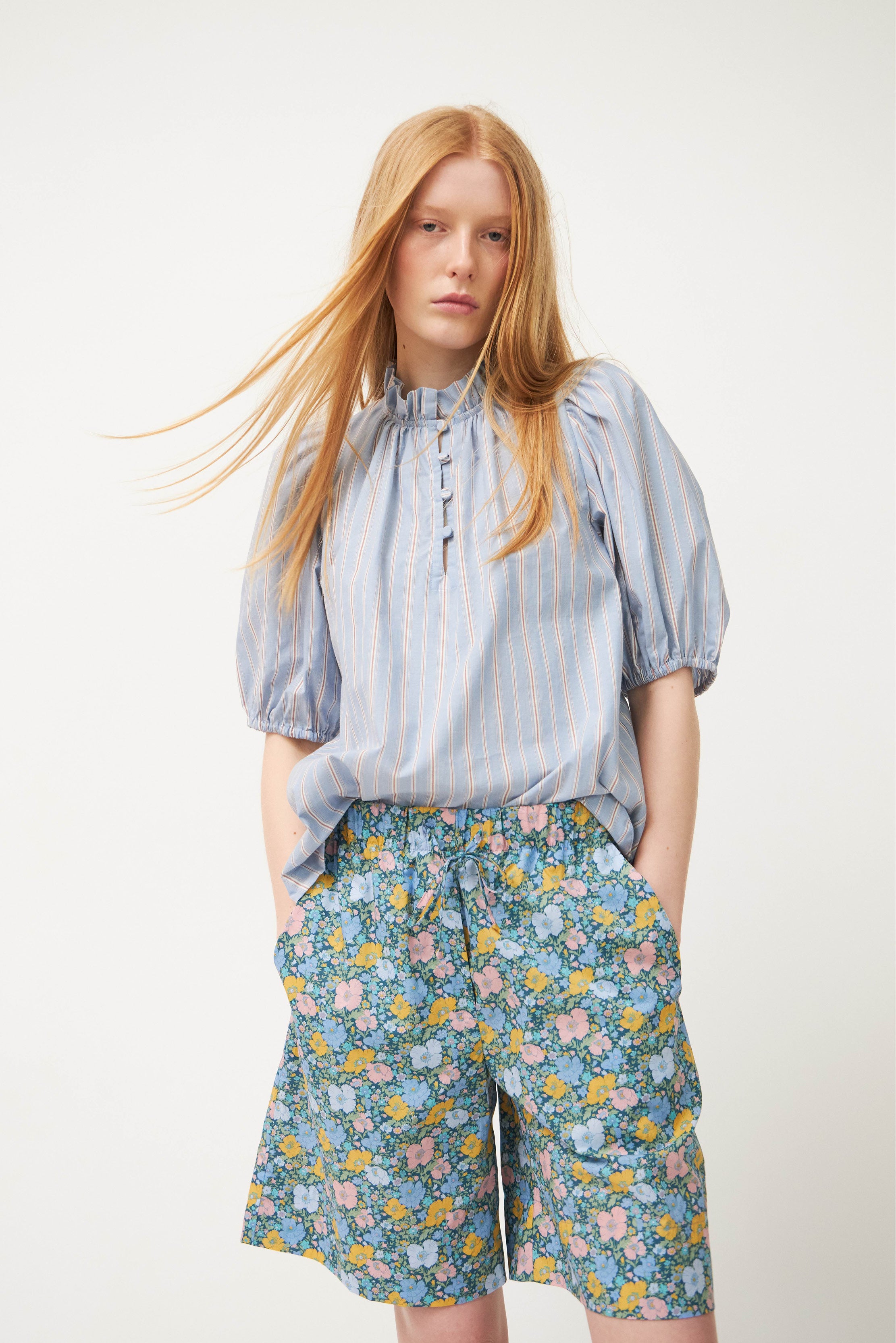 Woman wearing blue striped blouse and shorts with flower patterns