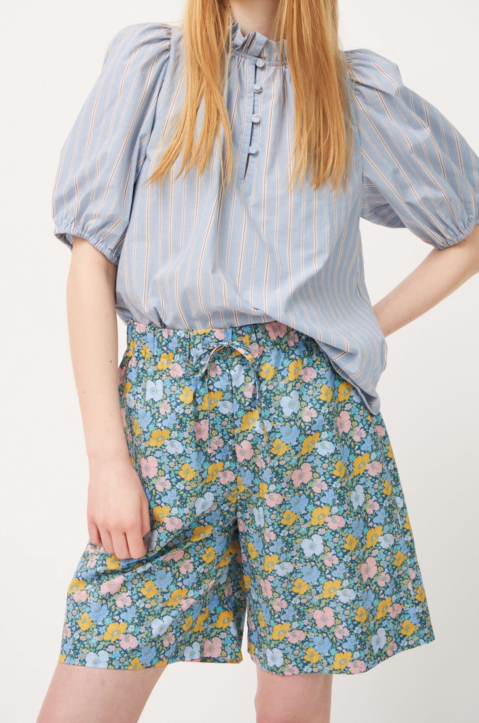 Woman in green cotton shorts with multi-colored floral print and striped short sleeved blouse
