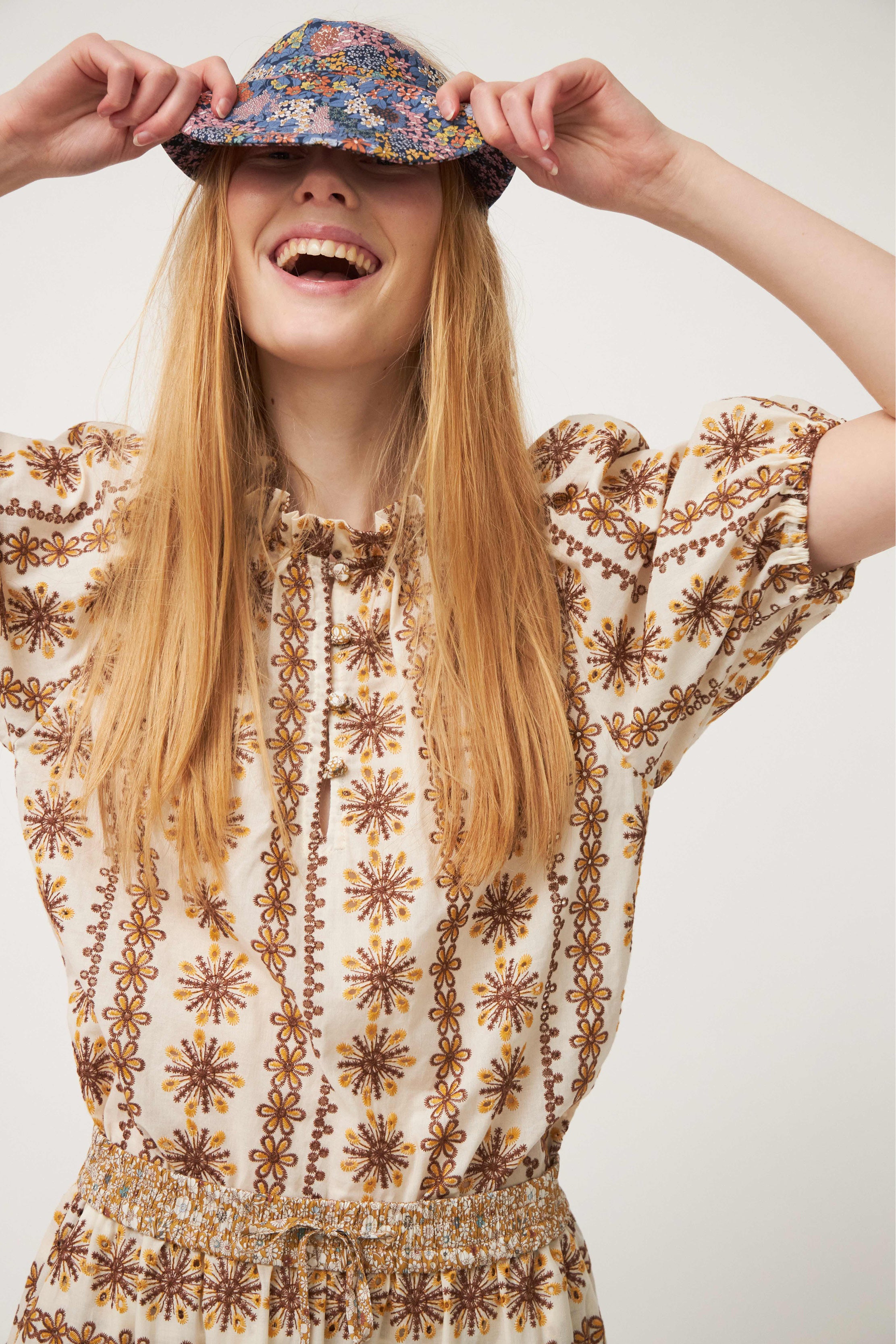 Woman in brown patterned blouse and flower hat