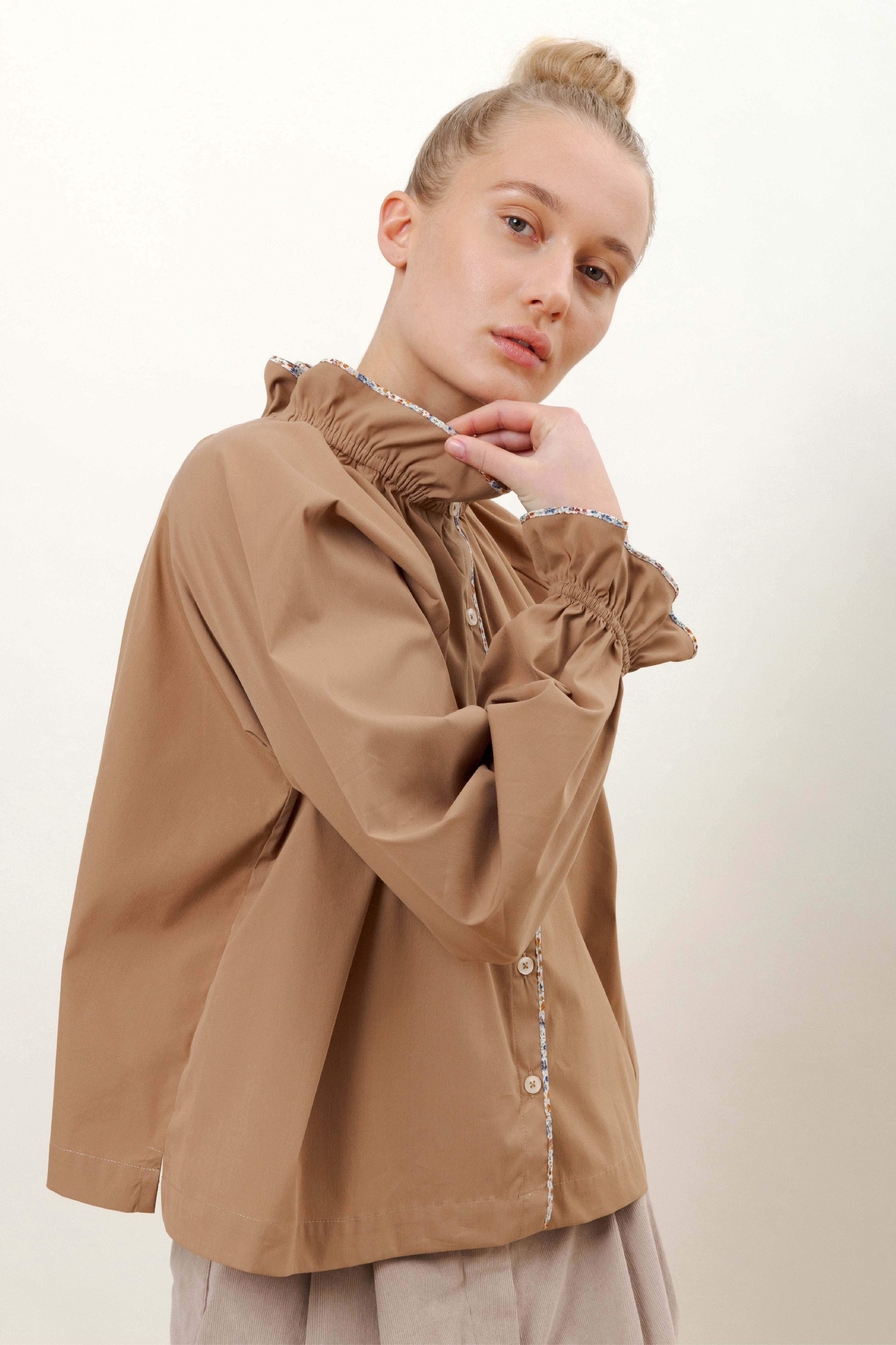Woman in brown shirt with long sleeves, buttons, pipings and ruffles