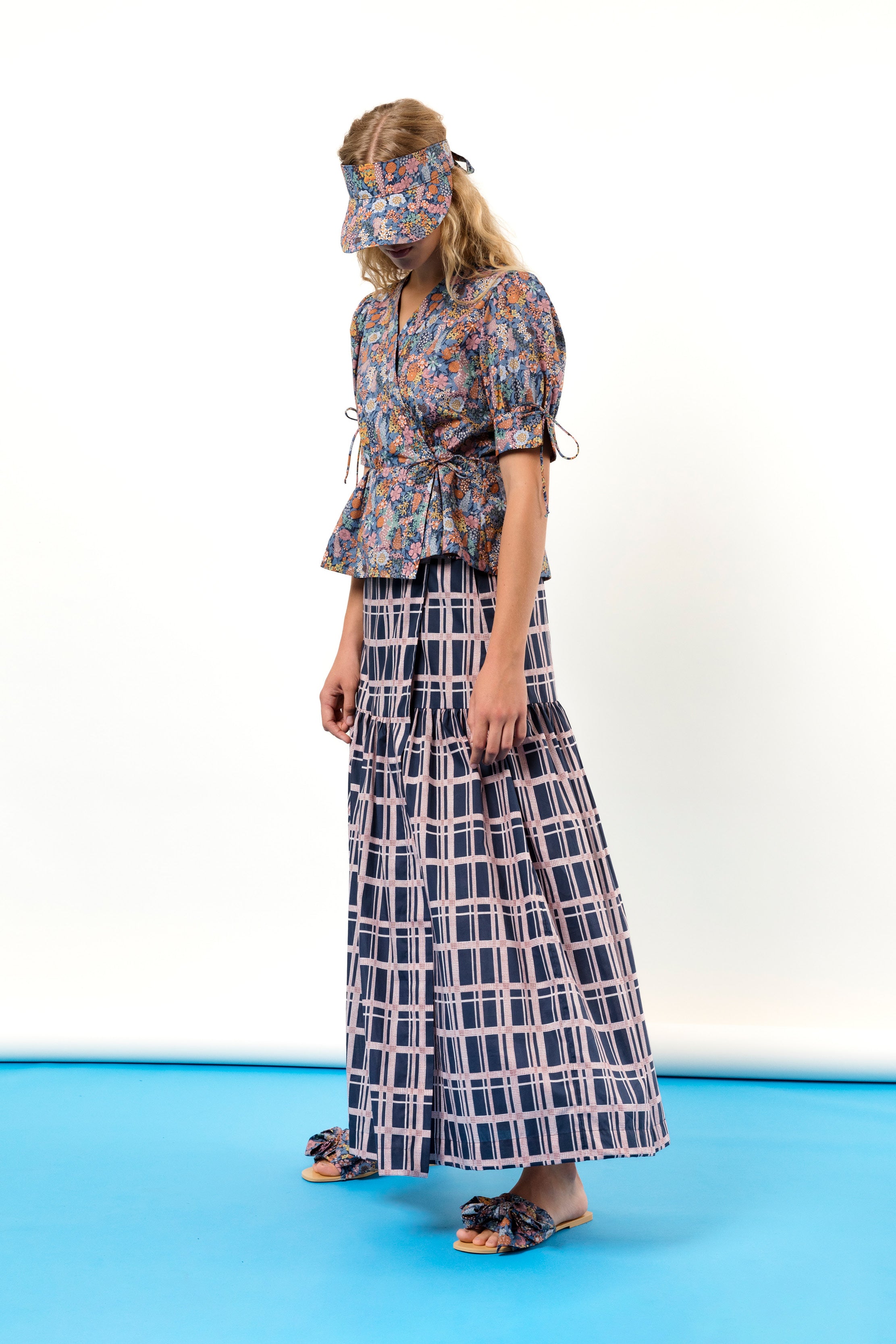 Woman in short sleeved wrap blouse and sun cap with flower pattern and checked maxi skirt