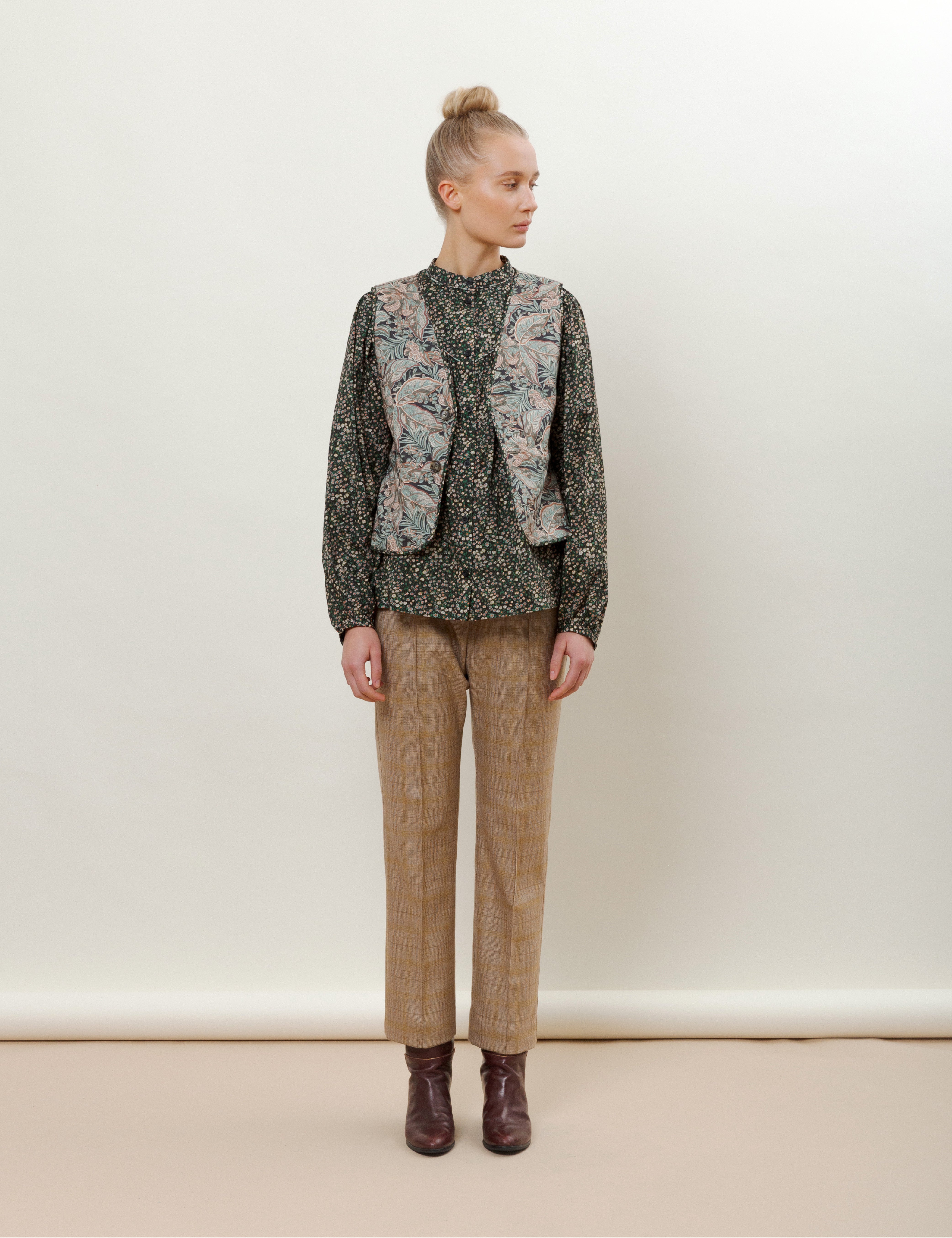 Woman with camel brown checked wool pants, green floral print long sleeved blouse and paisley patterned vest