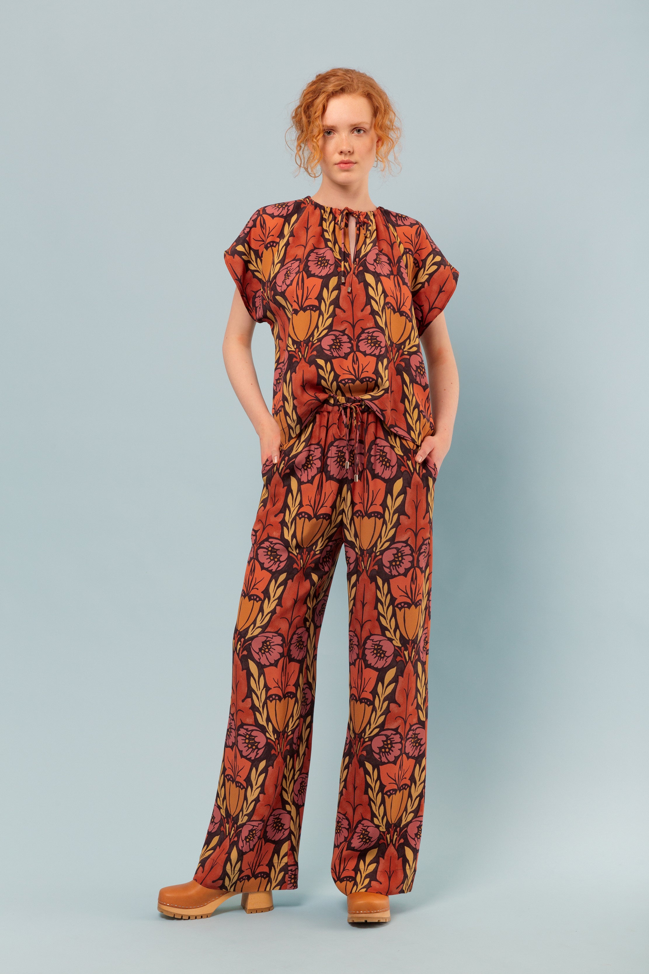 Woman in viscose pants and short sleeved top with large floral pattern in pink orange and yellow