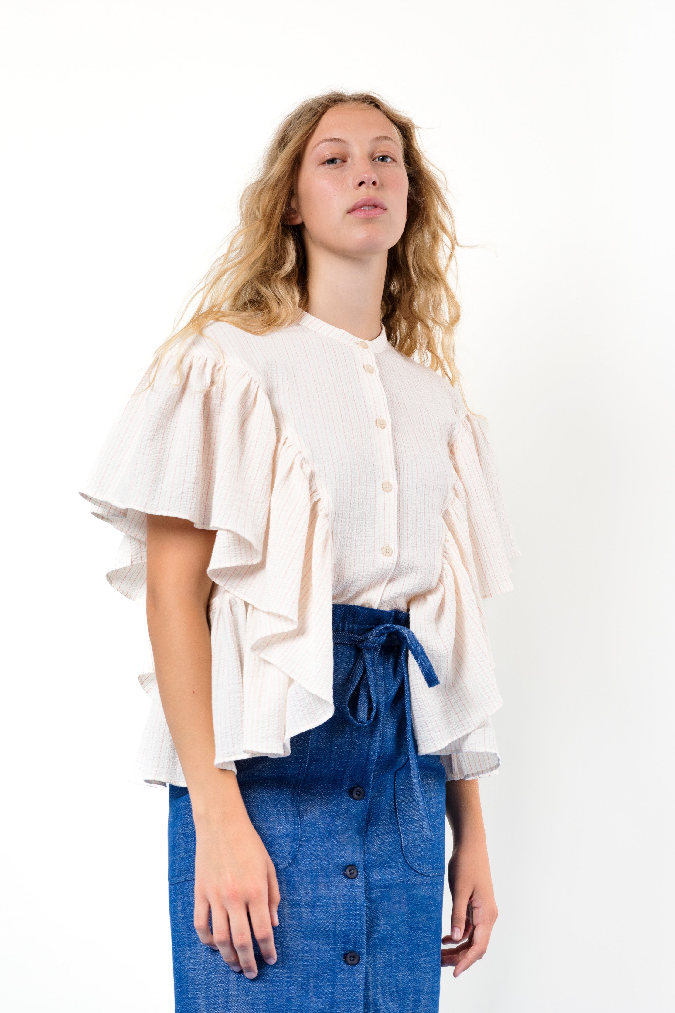 Woman in Pink short sleeved blouse with stripes and frills and blue skirt