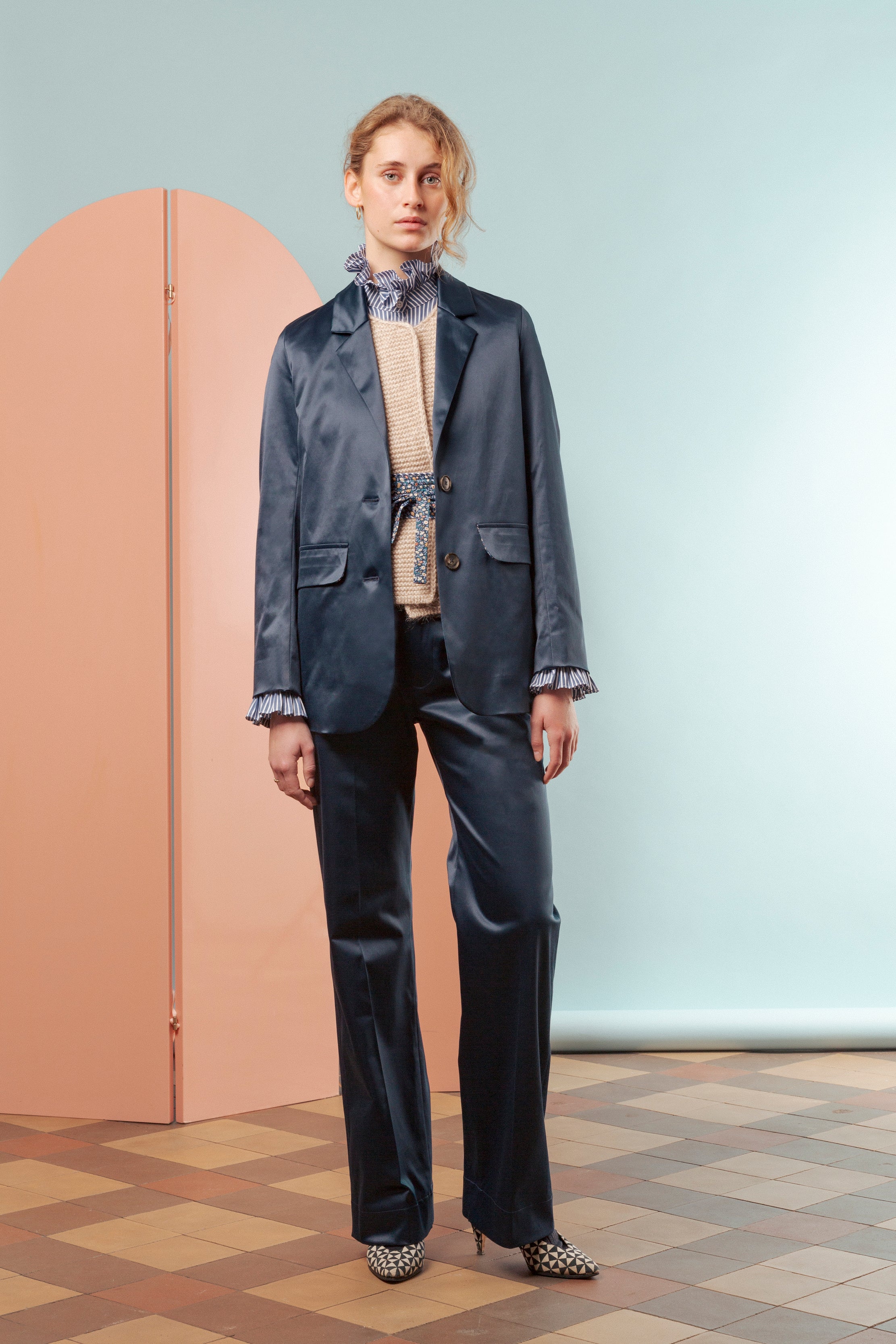 Woman in blue pants and jacket with buttons and pocket , vest and striped shirt with ruffled cuffs and collar