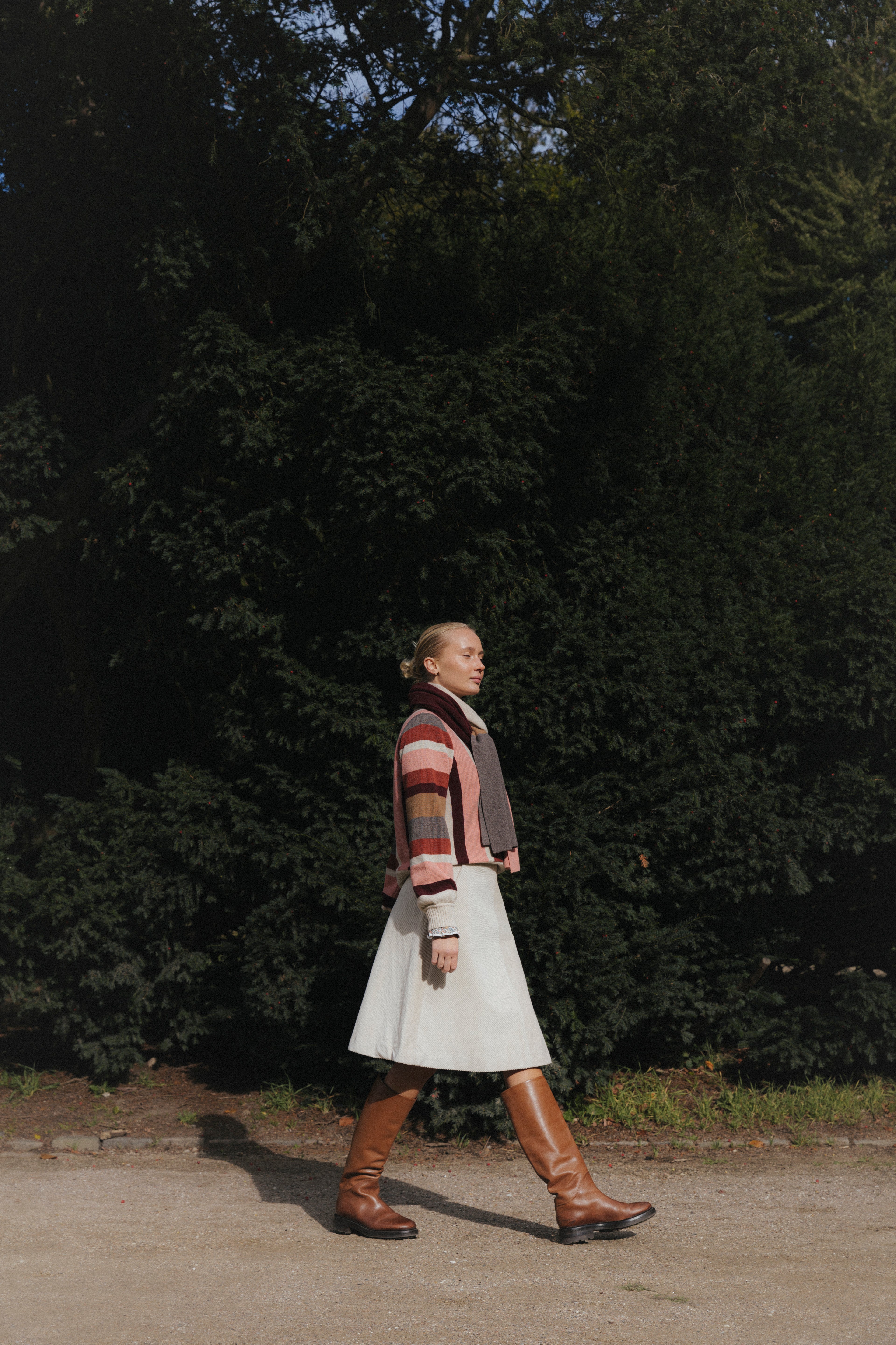Woman in creme colored corudroy skirt, striped sweater wool scarf and brown boots