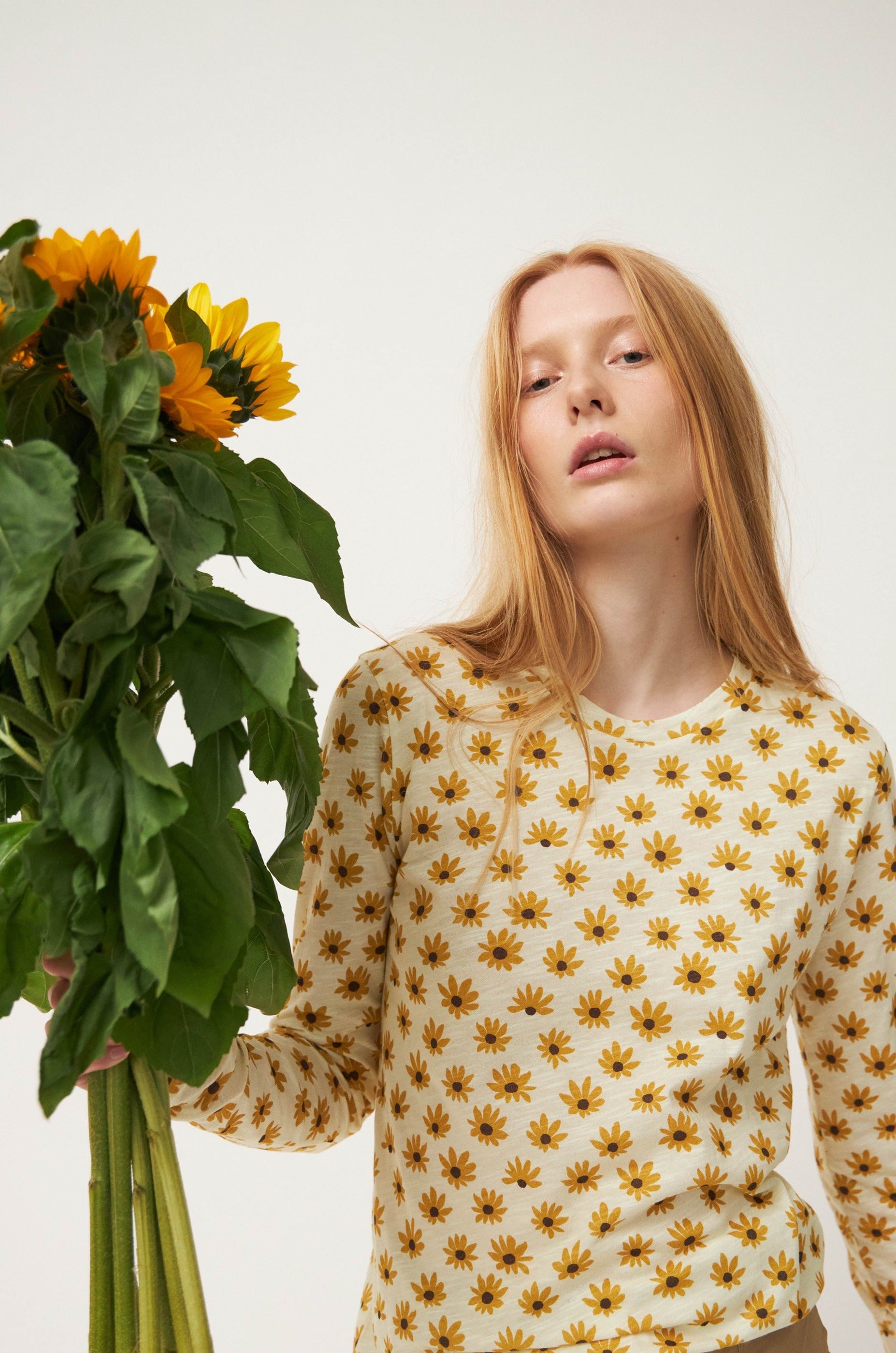 Woman in long sleeve t-shirt with sunflower pattern holding sunflowers