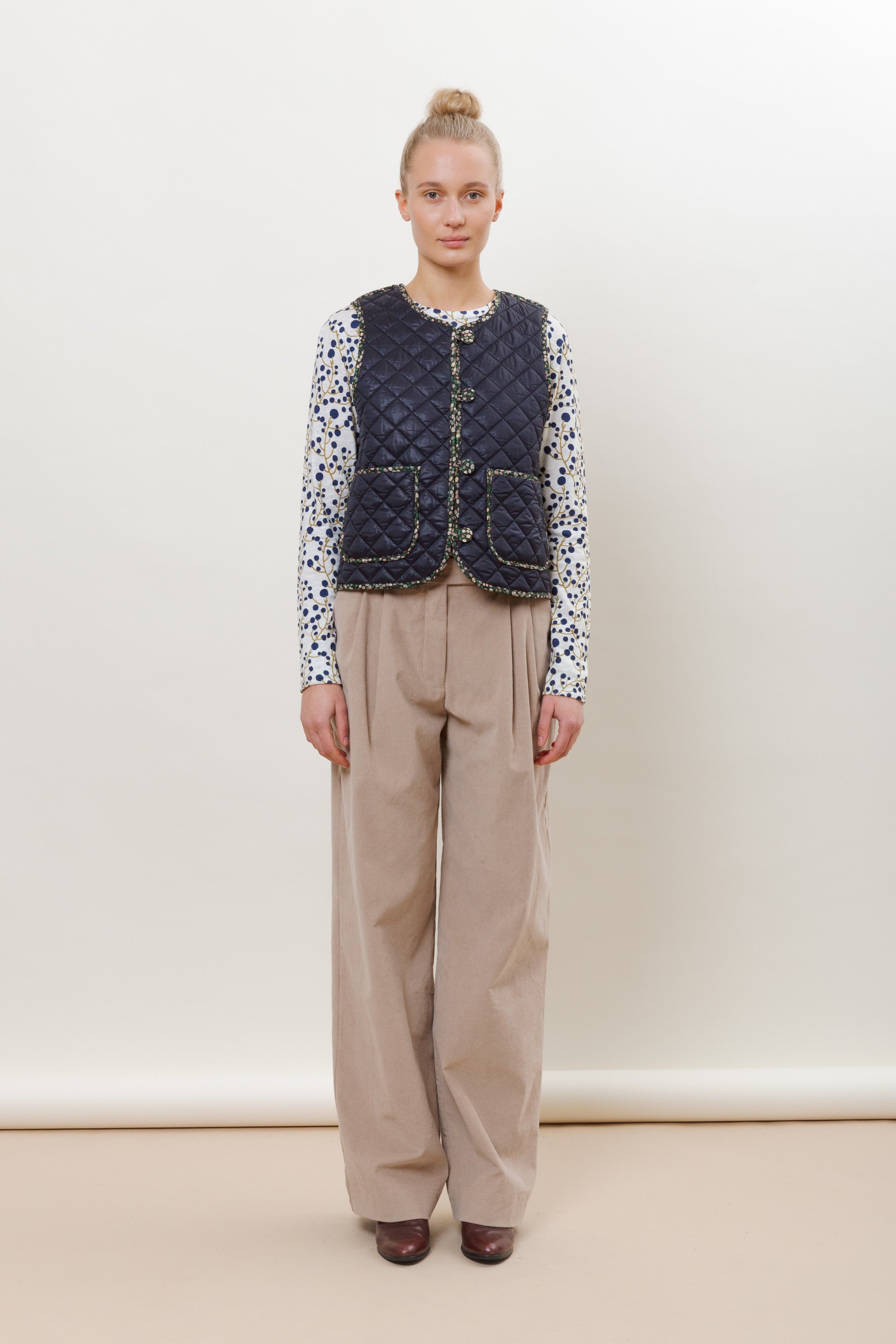 Woman in beige pants, long-sleeved patterned t-shirt and quilted blue vest with pockets