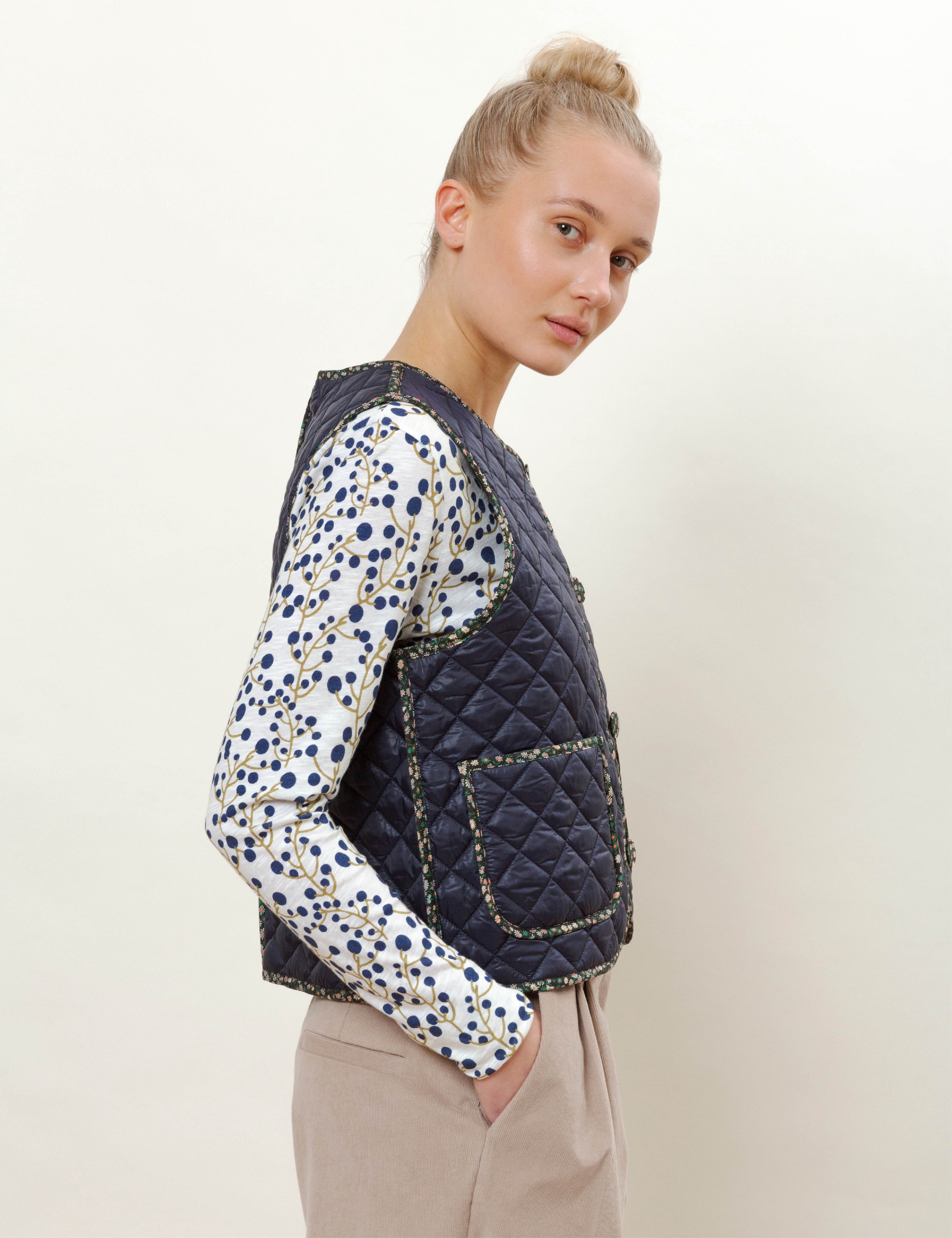 Woman in long-sleeved blueberry print t-shirt, blue quilt vest with buttons and pockets and beige corduroy pants
