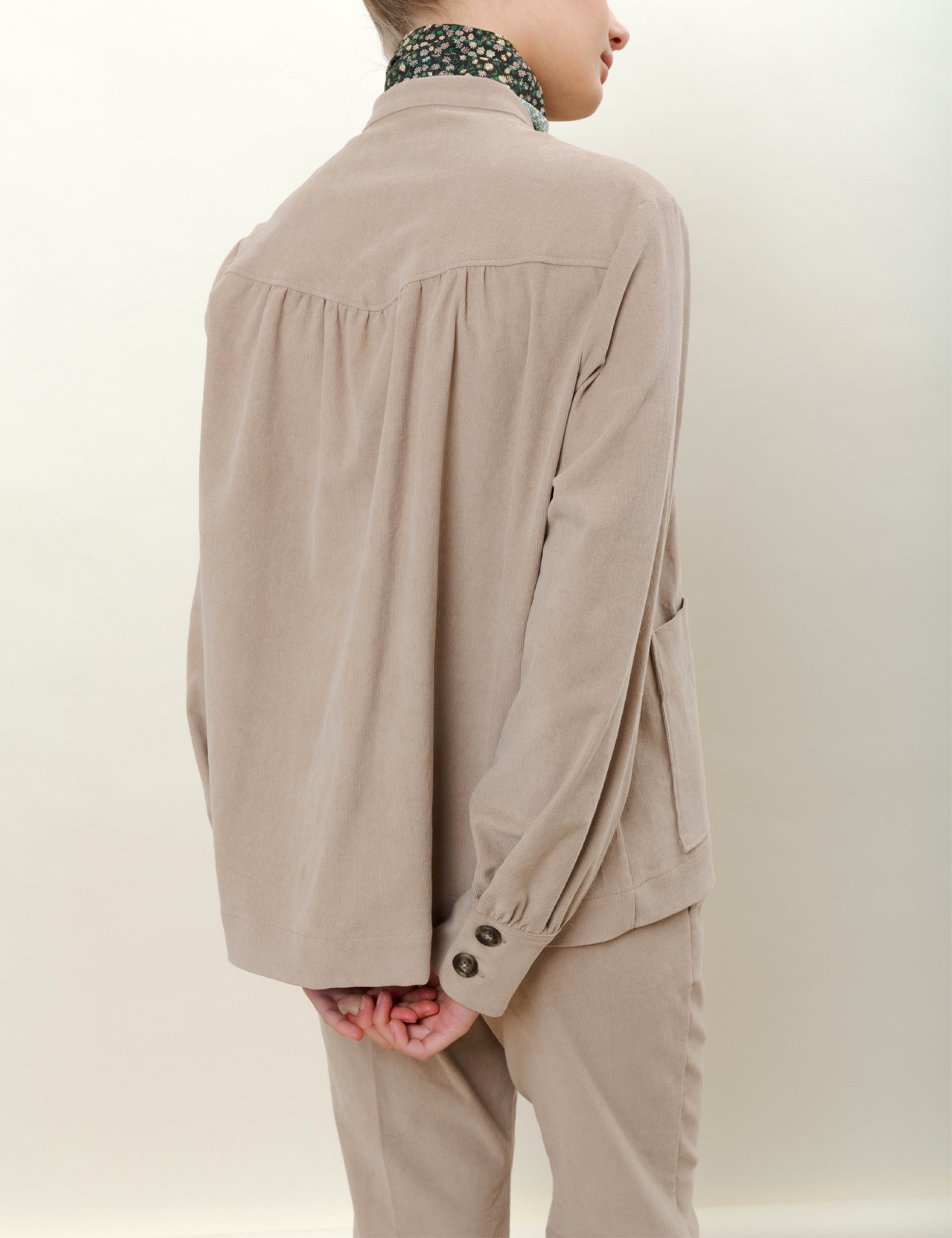 Woman in beige corduroy pants with cigarette silhouette and beige jacket with pockets and buttons