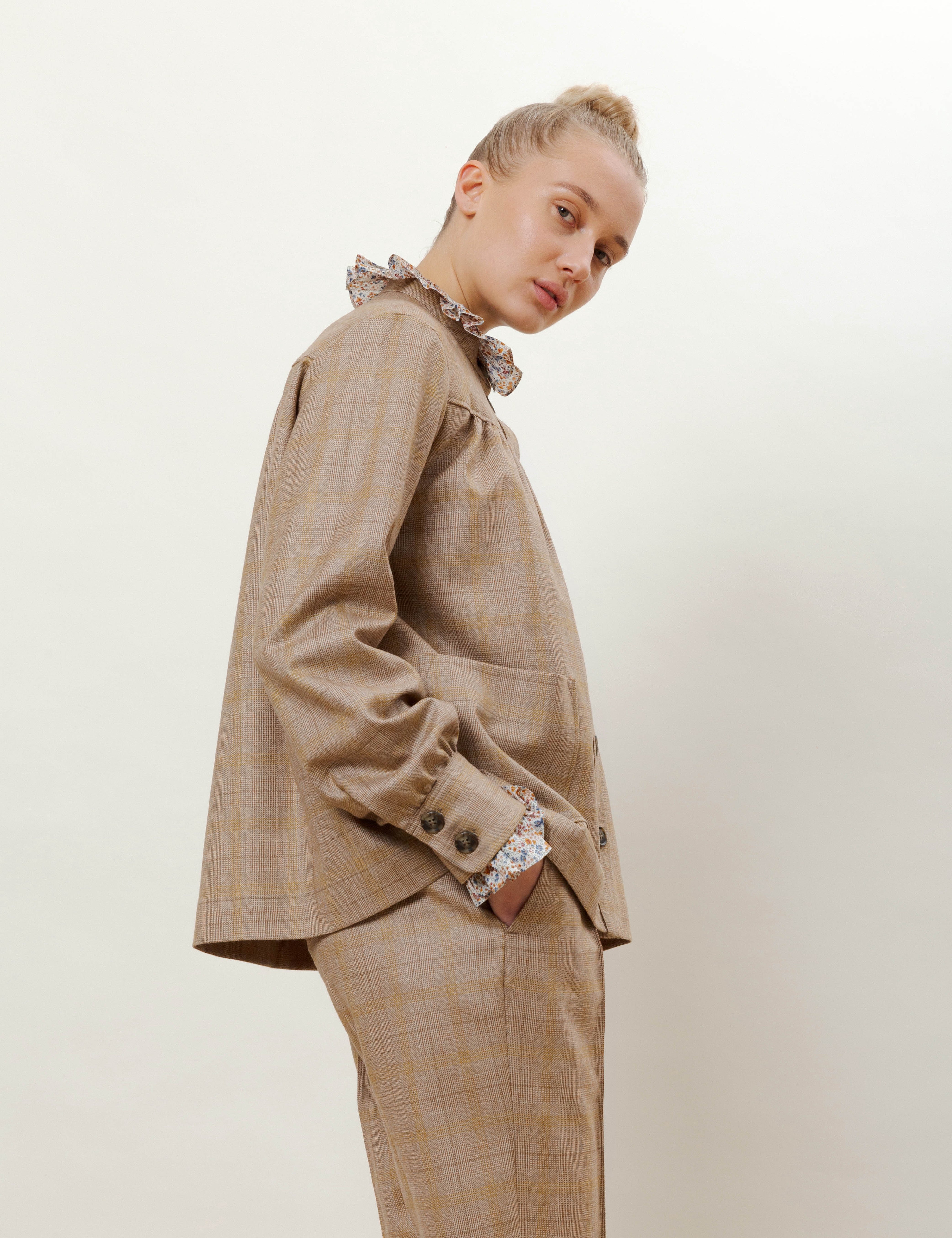 Woman in beige check print wool pants and jacket with buttons and pockets and shirt with frills