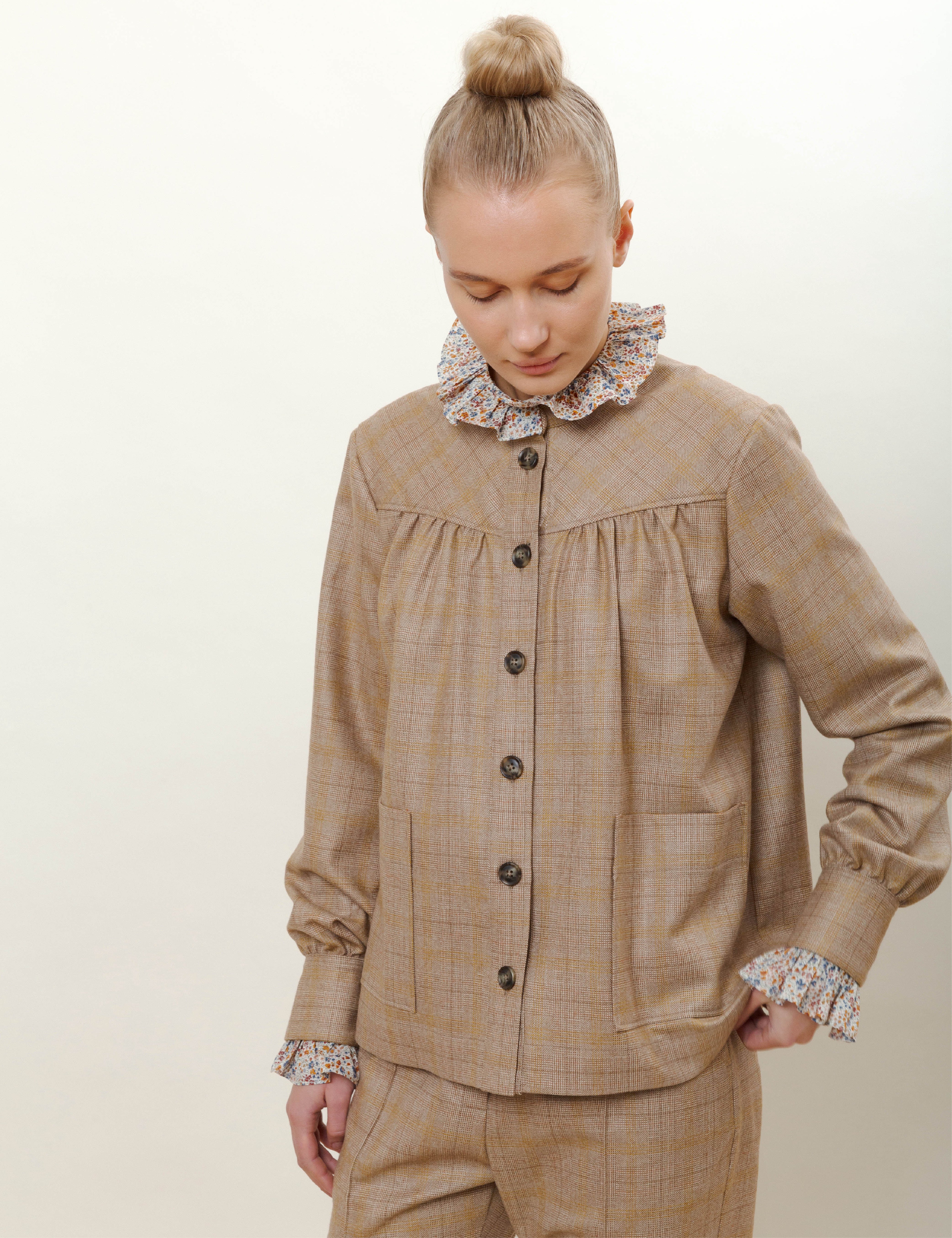 Woman in beige check print wool pants and jacket with buttons and pockets and shirt with frills