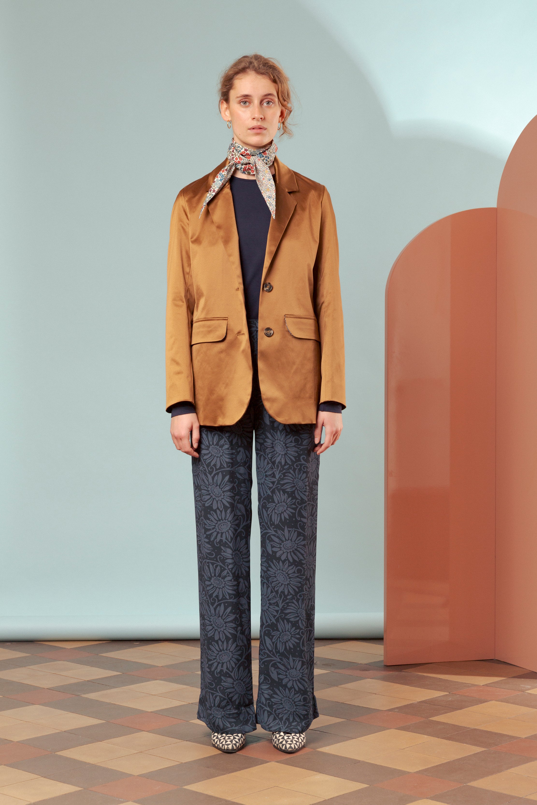 Woman in brown jacket with pockets and buttons, blue patterned pants and bandana