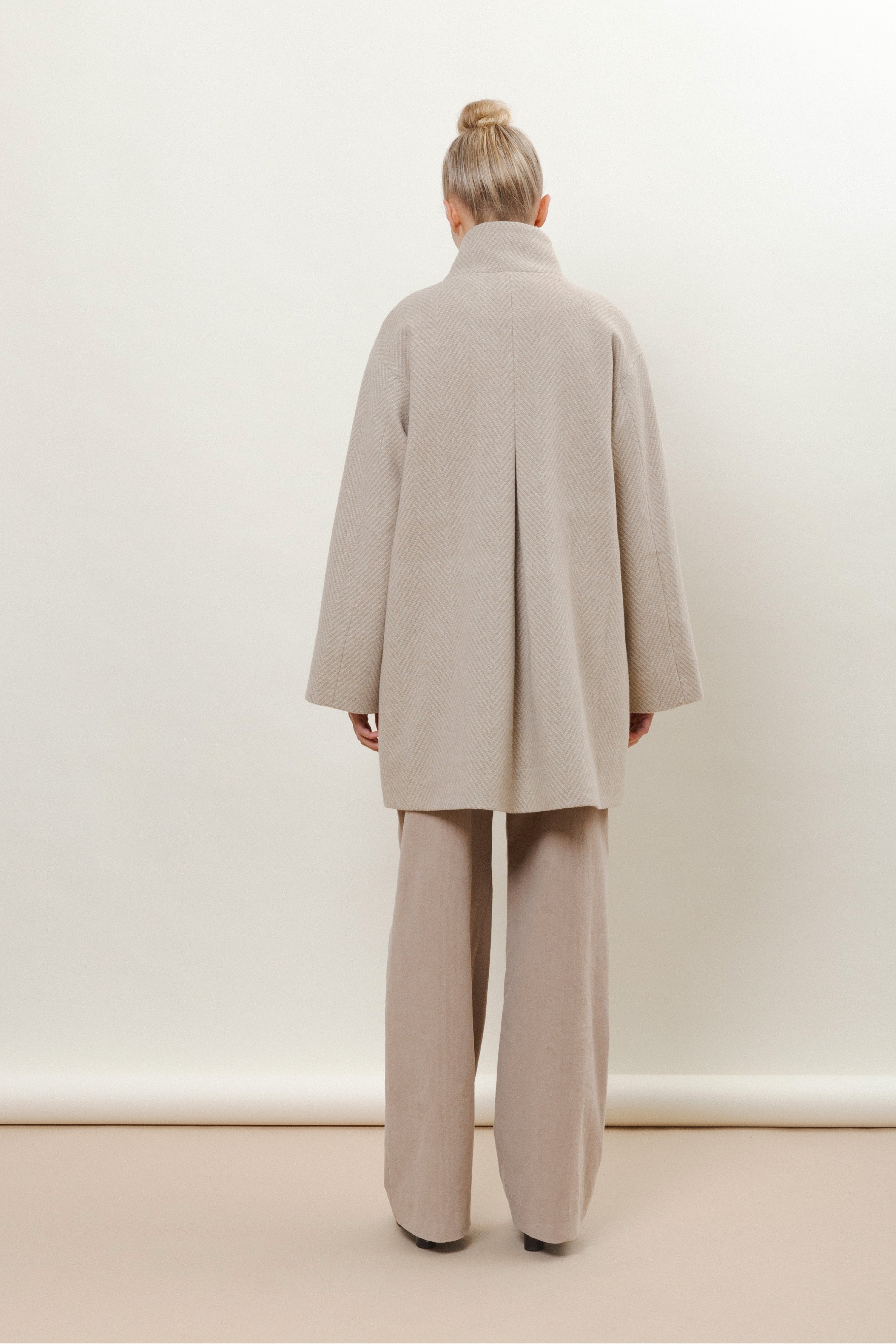 Woman in beige herringbone patterned wool jacket with stand collar and beige pants