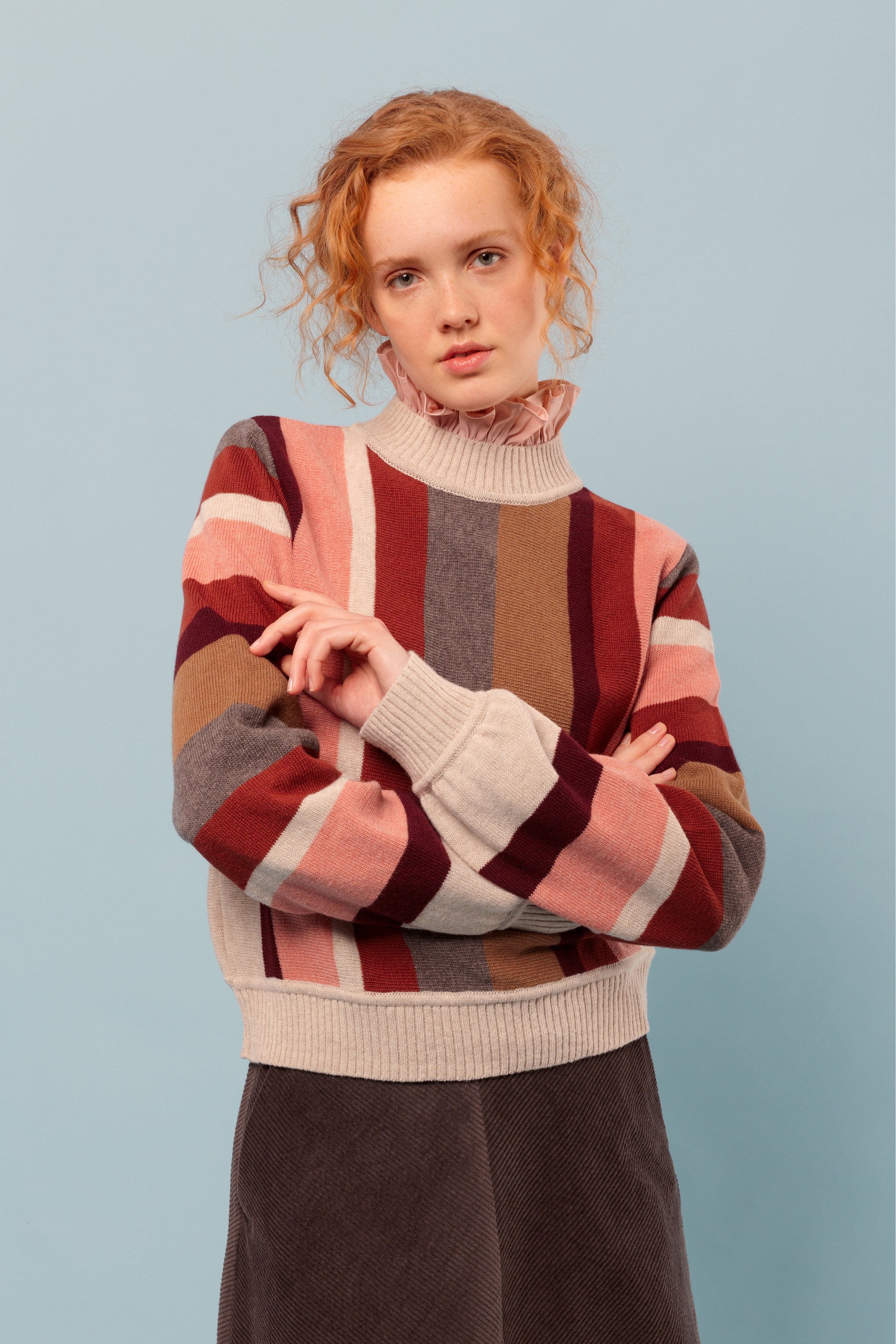 Woman in Striped wool pullover in pink, beige, brown and red, frilled pink blouse and brown skirt