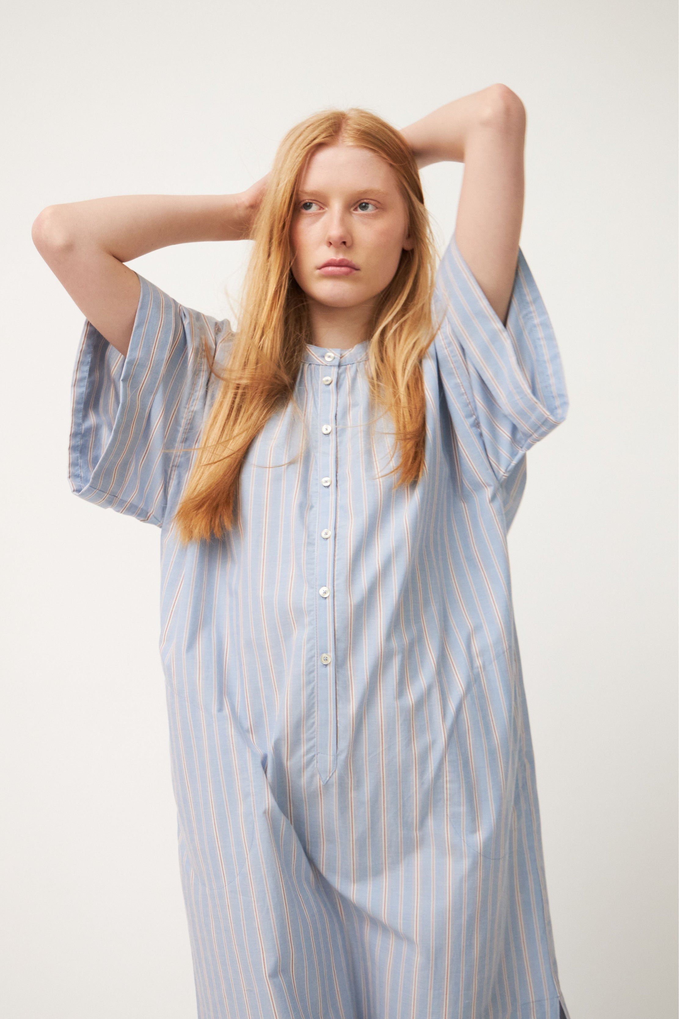 Model wearing blue white and red striped kaftan dress with short sleeves and buttons