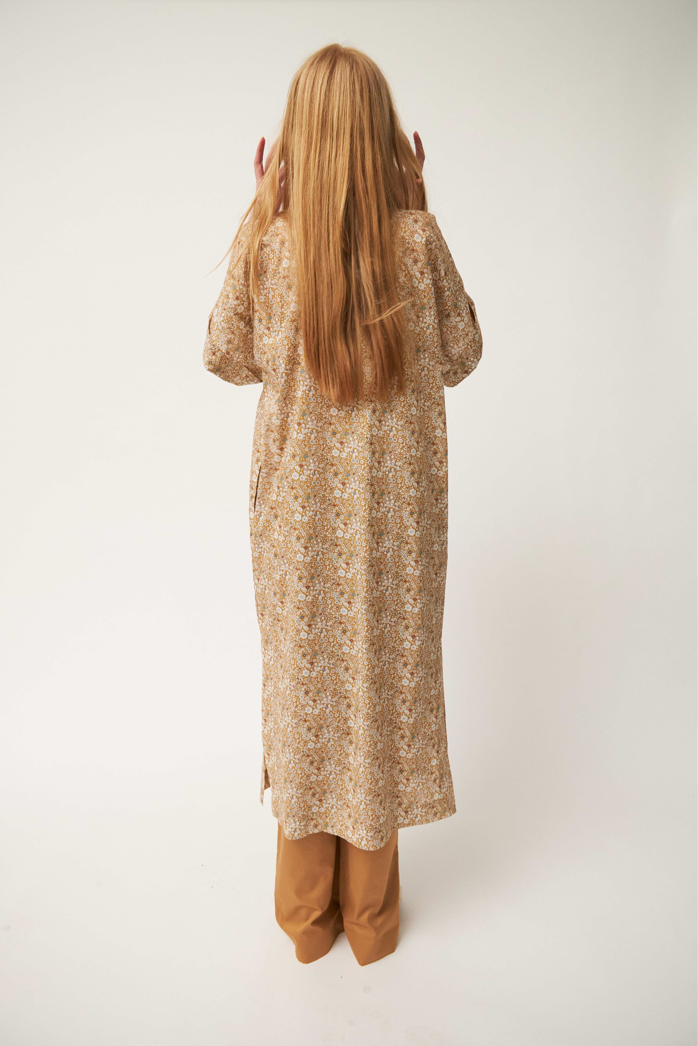 Model wearing white and brown flower patterned kaftan dress with short sleeves and buttons and brown pants
