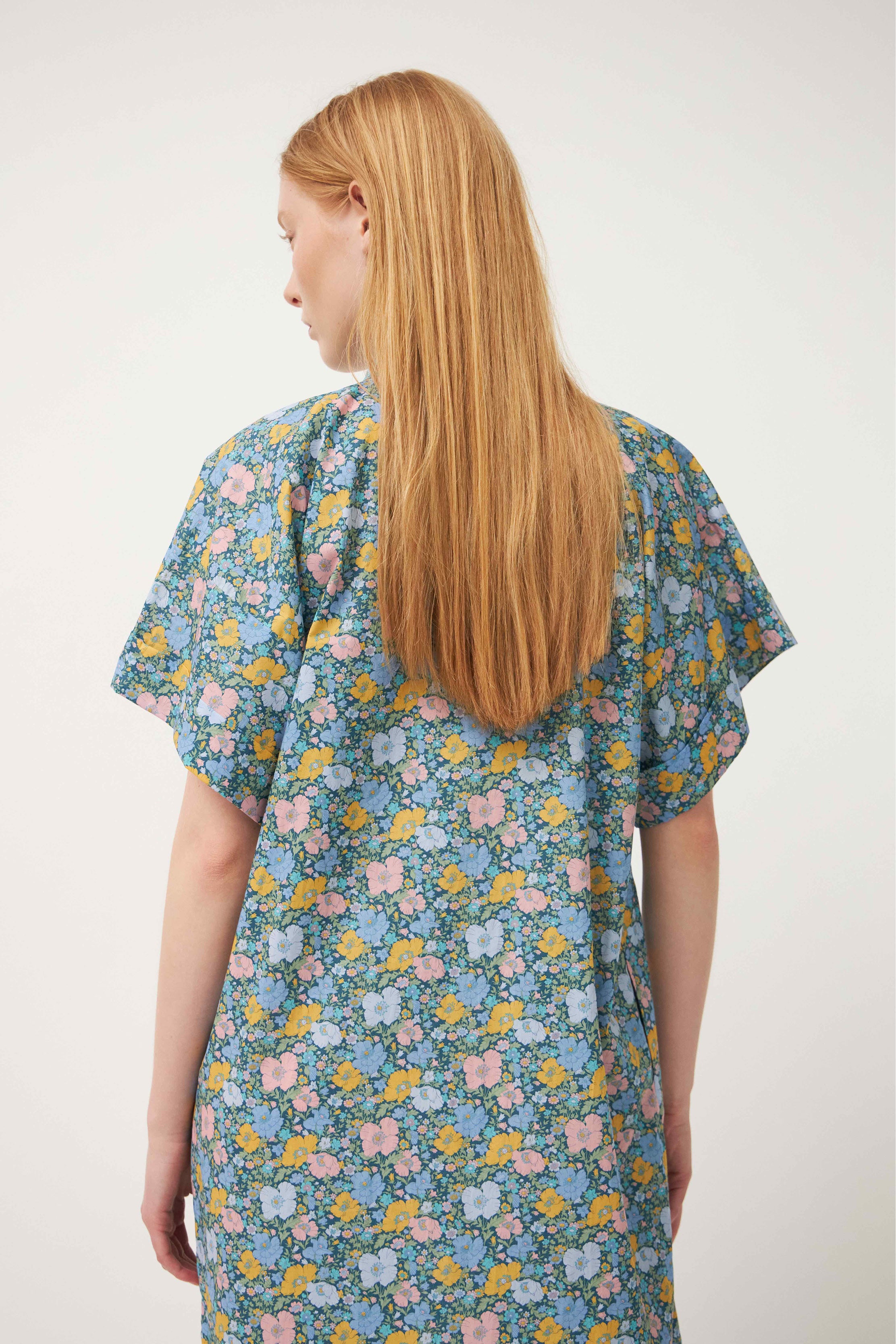 Woman in green multi colored flower patterned kaftan dress with short sleeves and buttons