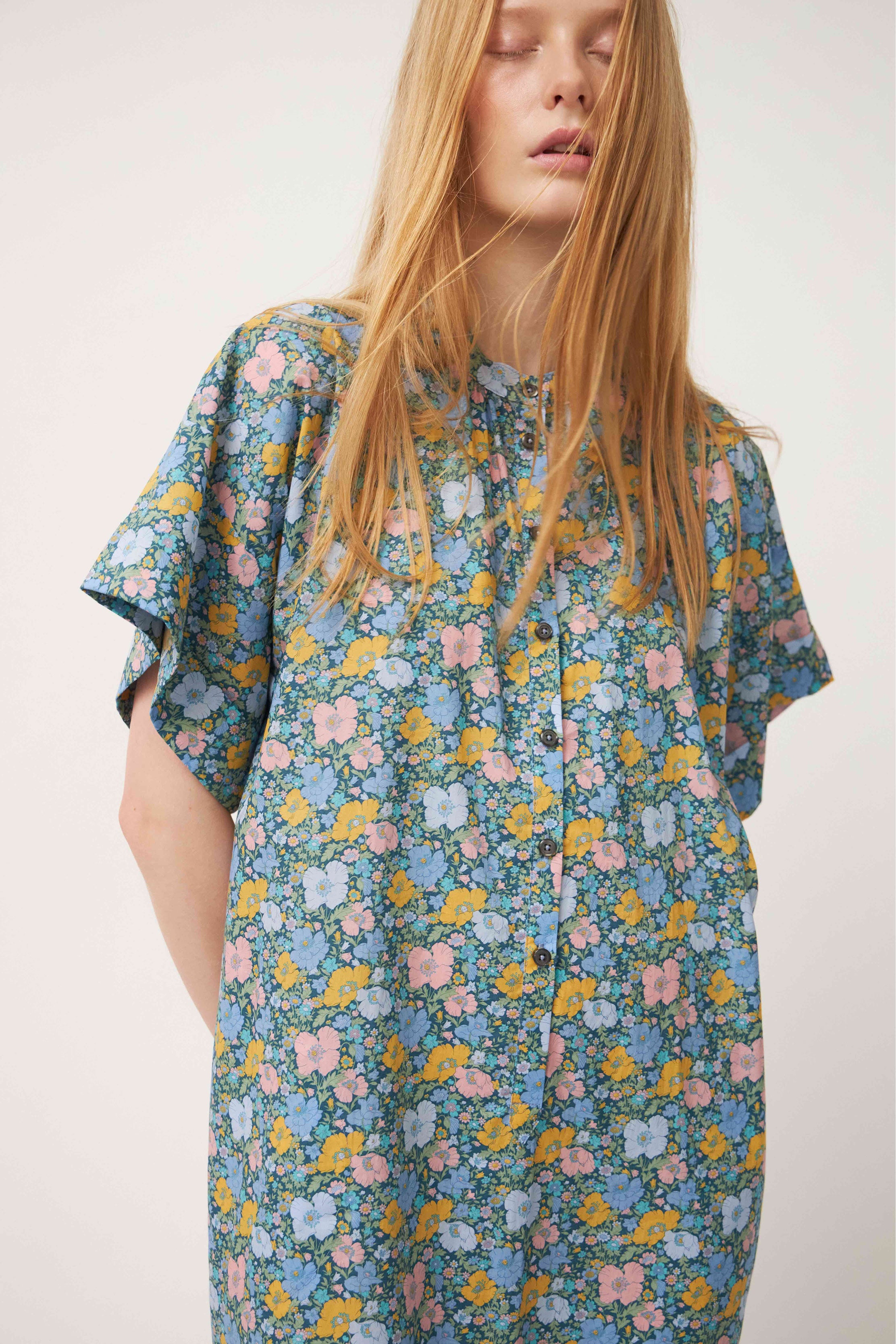 Woman in green multi colored flower patterned kaftan dress with short sleeves and buttons