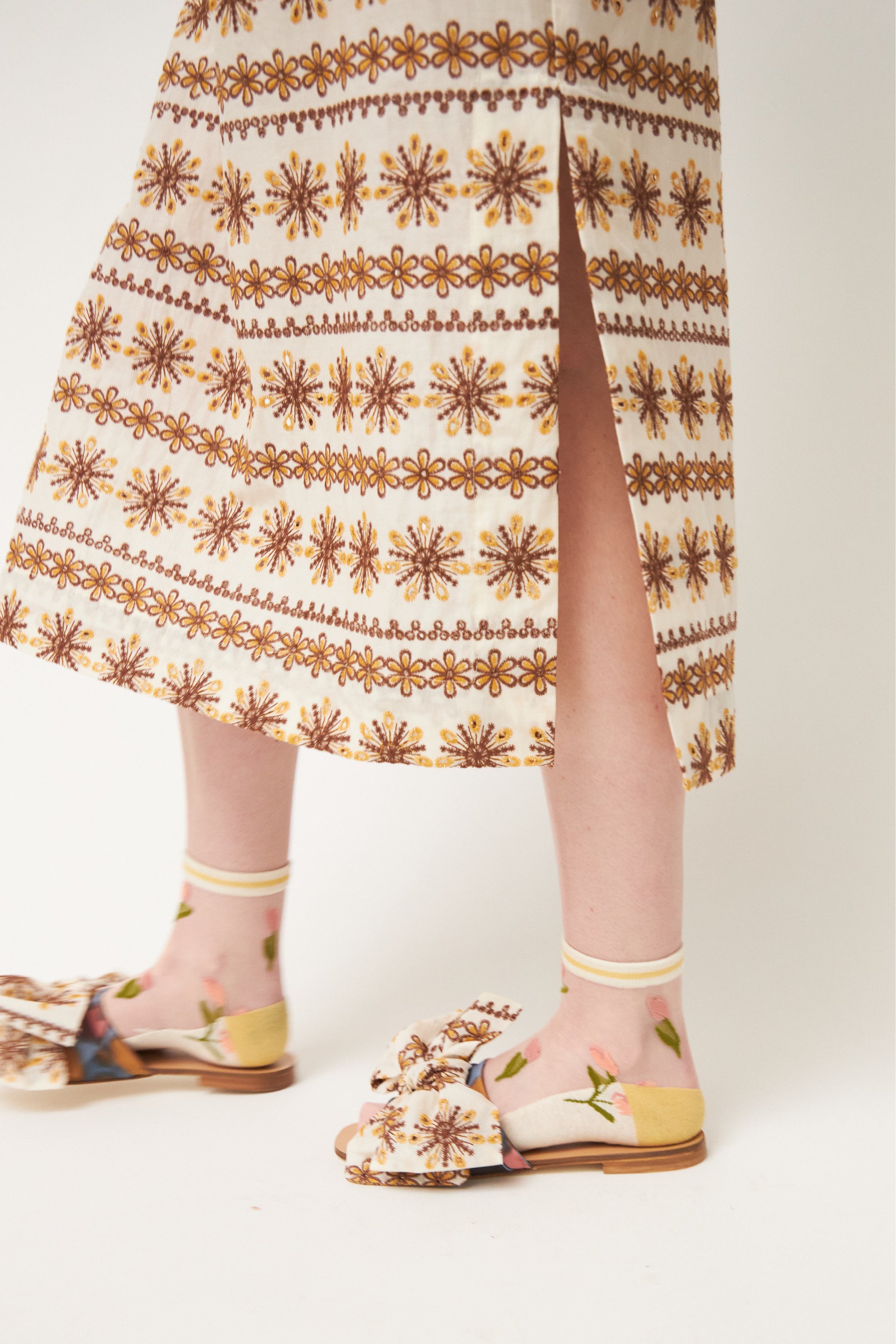 Laced white and brown patterned kaftan dress with short sleeves and buttons, flower patterned socks and sandals with bows