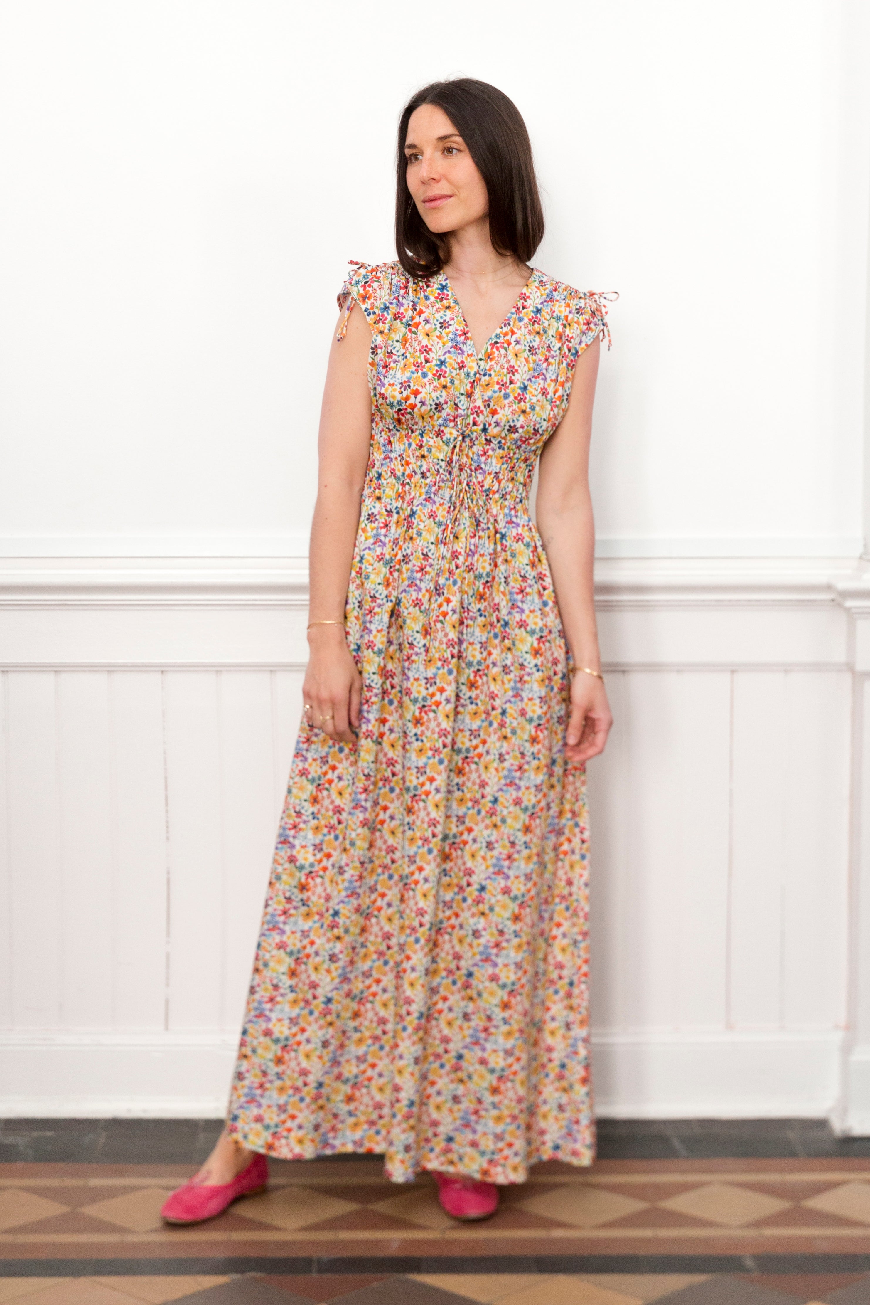 Woman in sleveless multi colored flower patterned maxi dress and red shoes