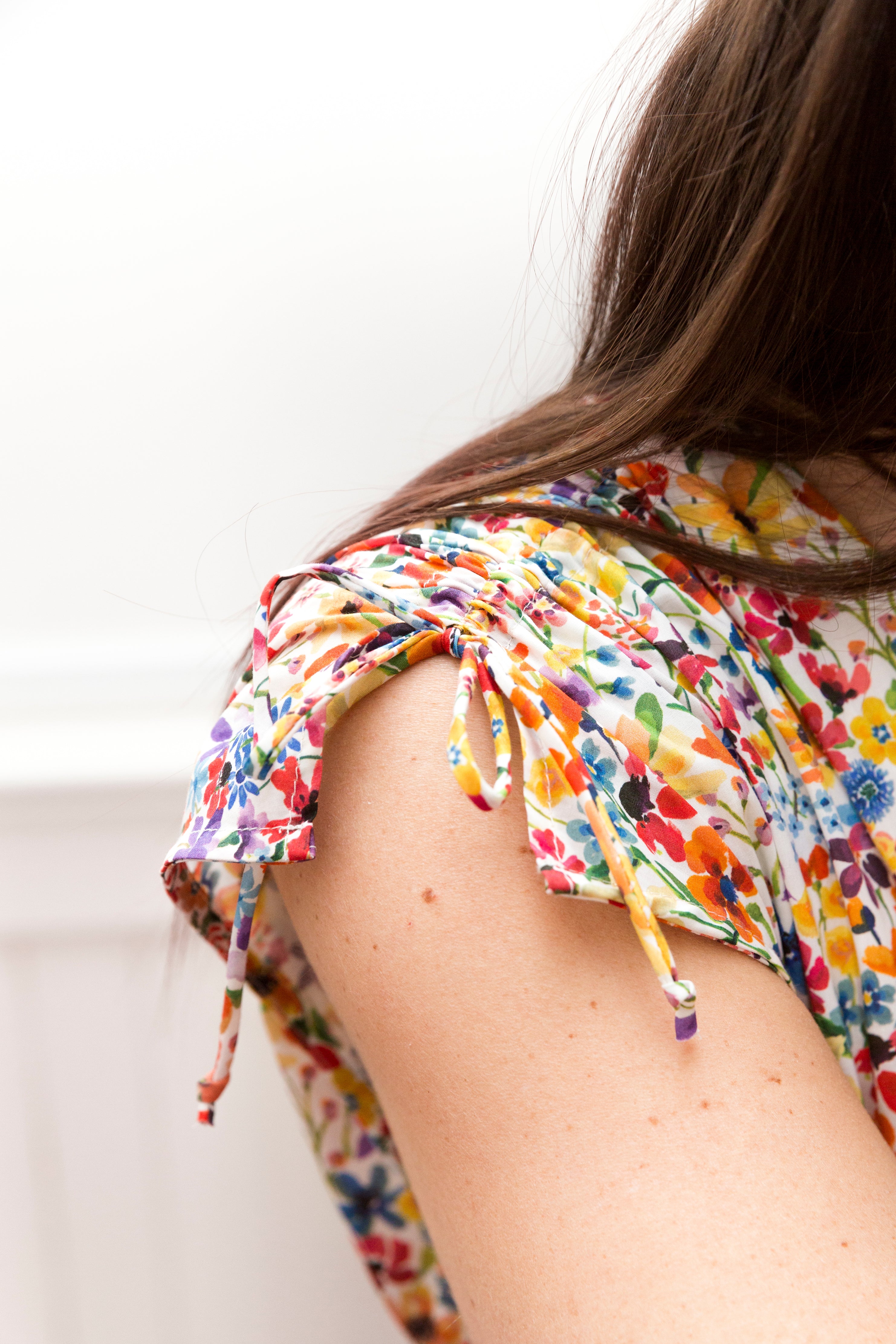 Dark hair and detail from sleveless multi colored flower patterned maxi dress