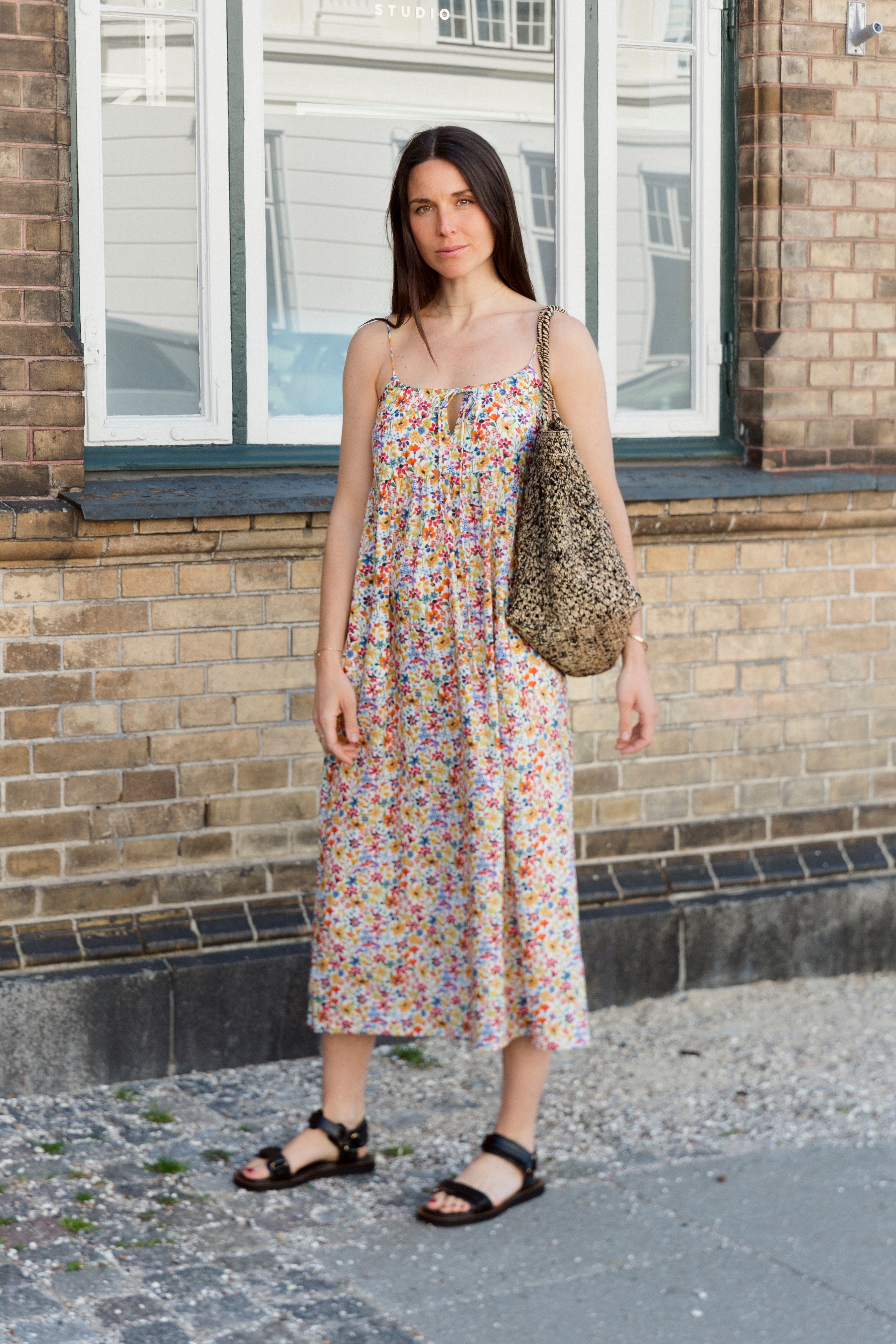 Woman in strap dress with multi colored flower pattern, shoulder bag and black sandals
