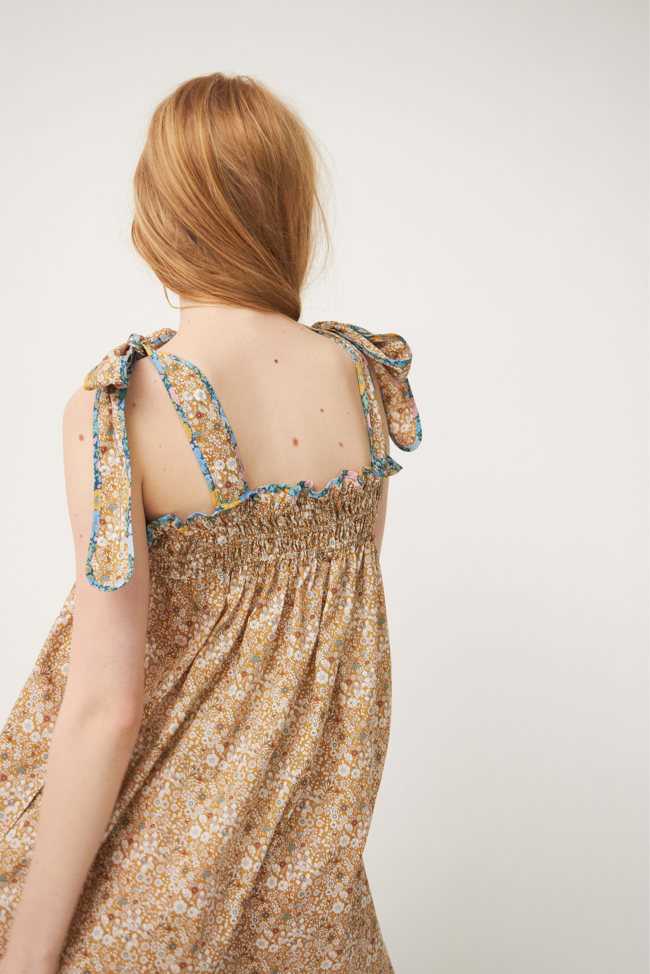 Woman in strap dress with beige and brown flower pattern and shoulder bows