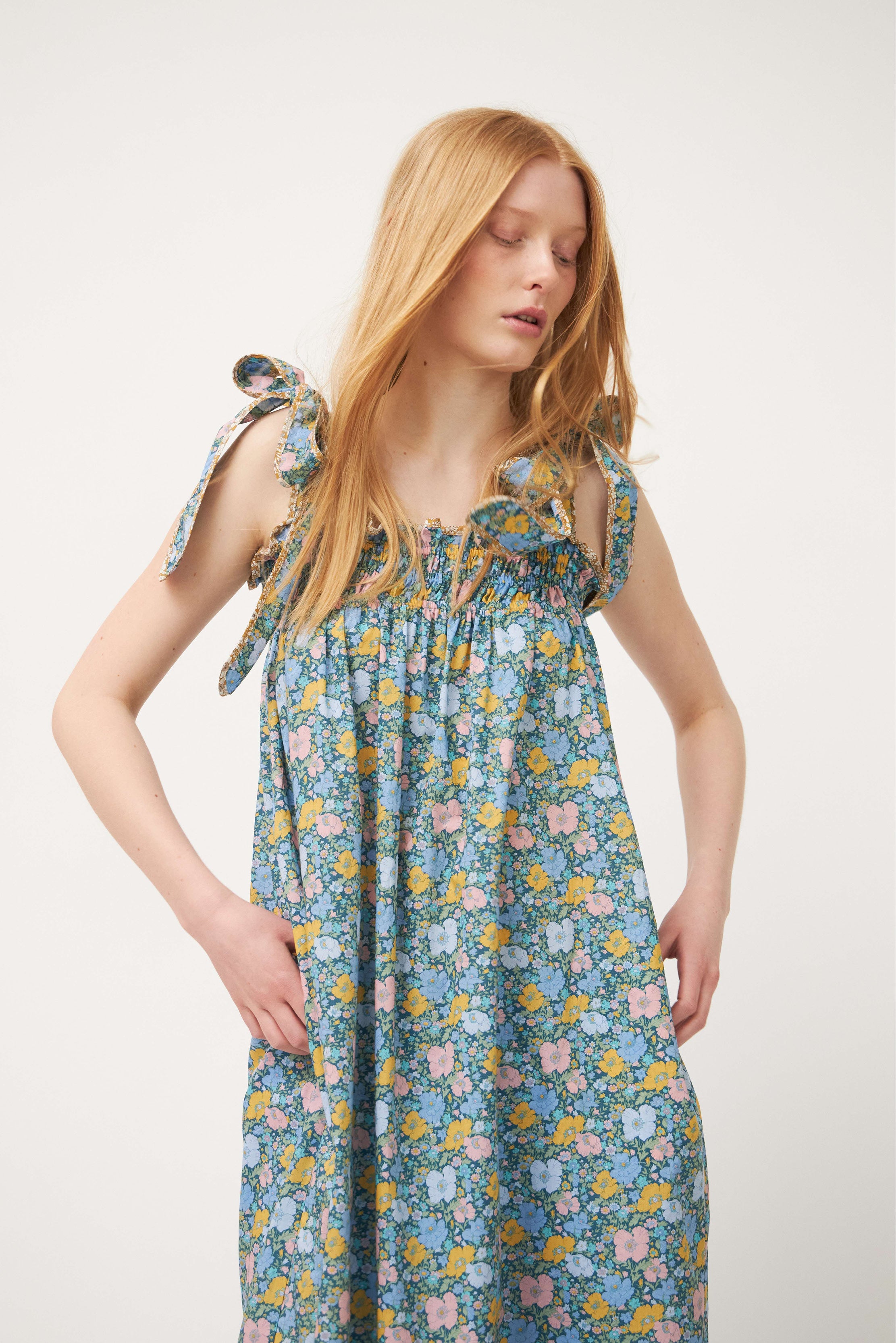 Woman in strap dress with green and multi colored flower pattern and shoulder bows