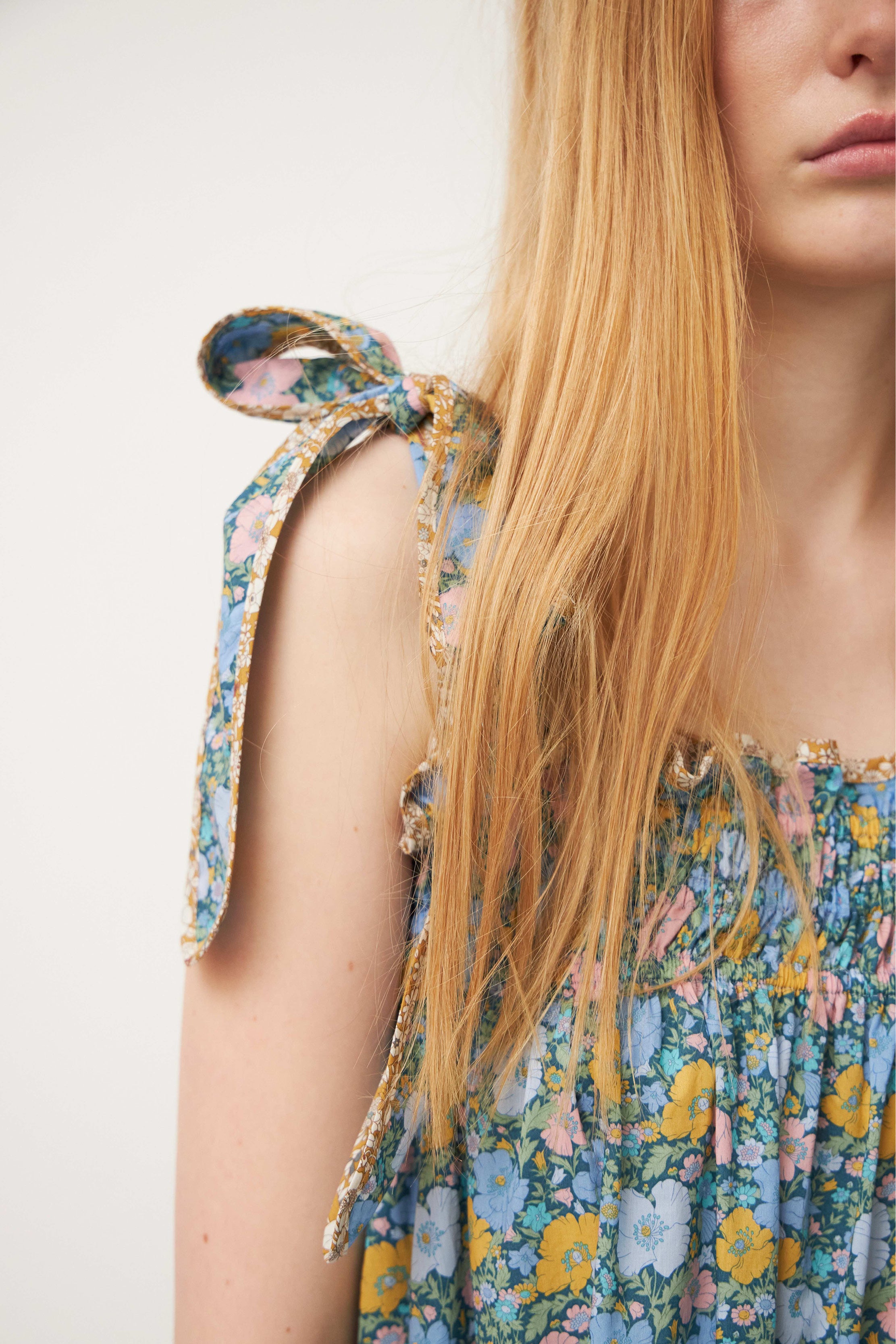 Woman in strap dress with green and multi colored flower pattern and shoulder bows