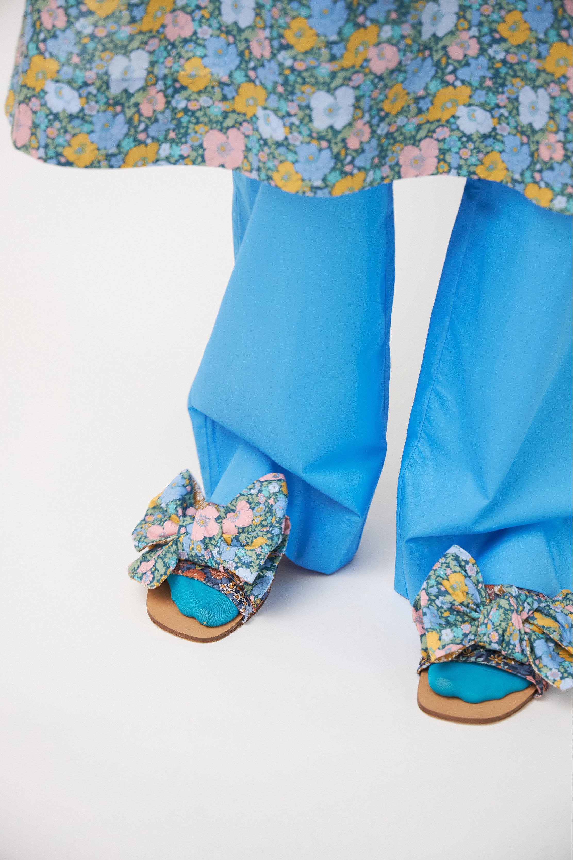 Dress with green and multi colored flower pattern and shoulder bows, blue trousers and sandals with bows