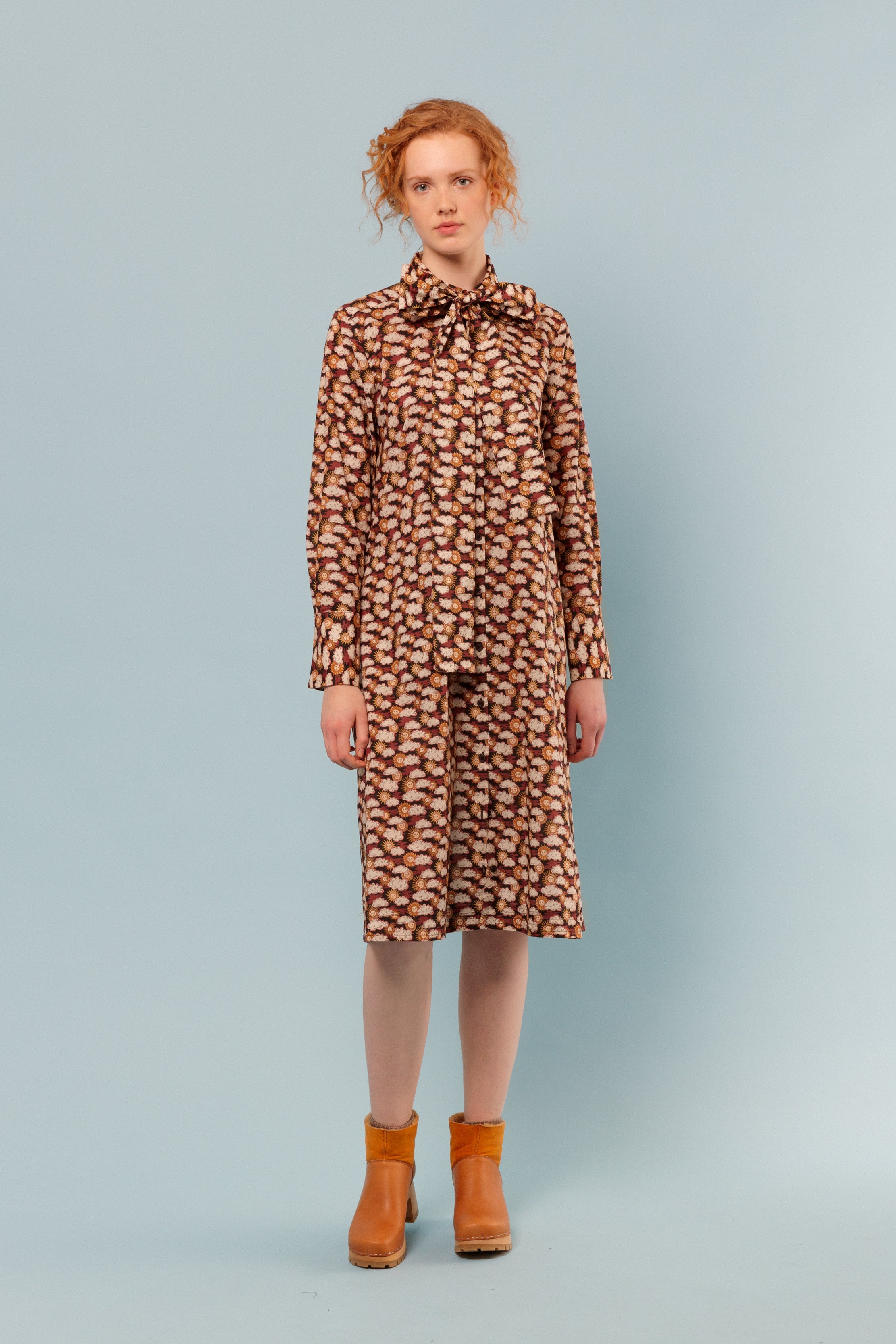 Woman wearing cotton shirt dress with sun and clouds pattern, long sleeves, bow around neck and orange boots