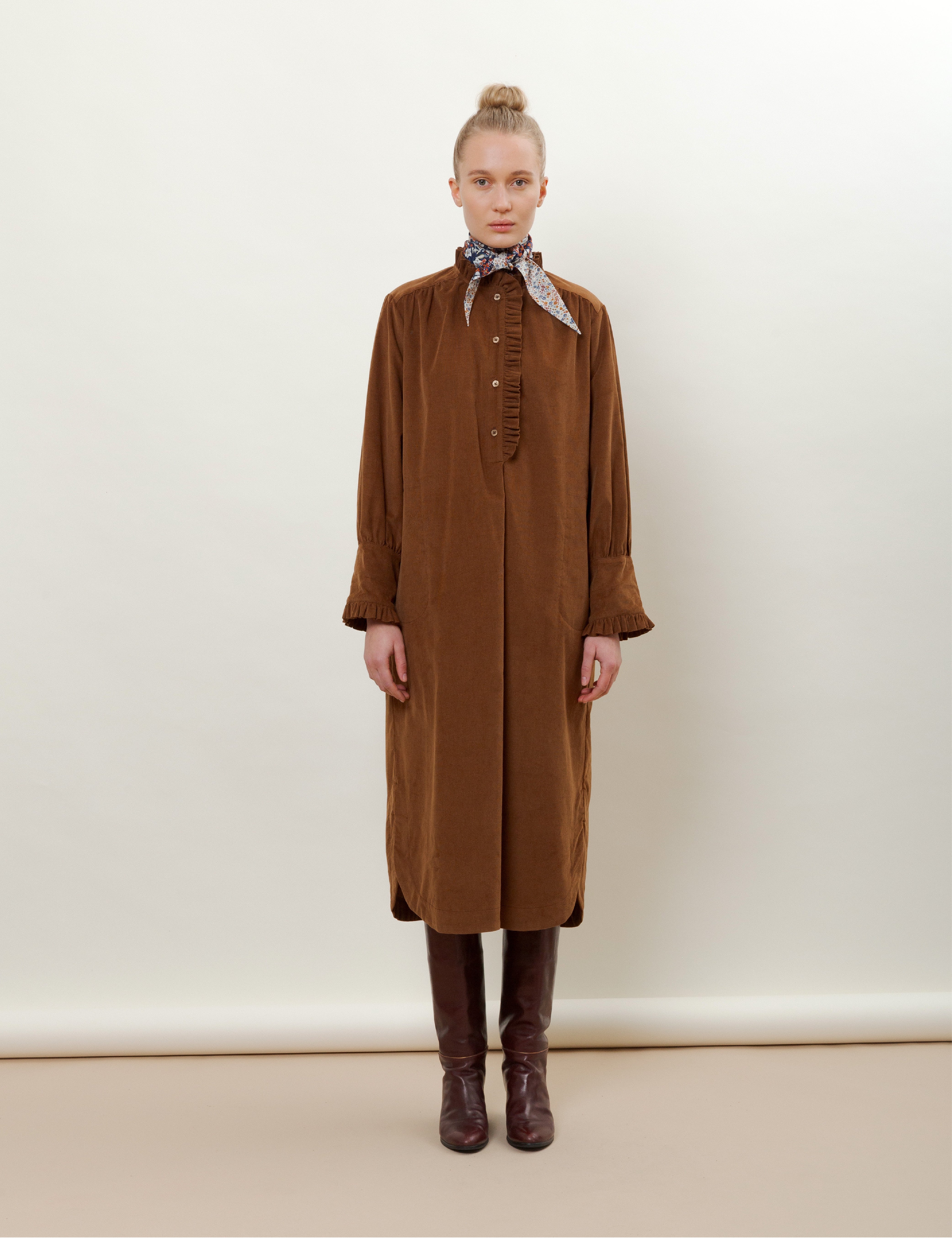 Woman in brown corduroy dress with buttons and frills on the front and flower patterned bandana scarf