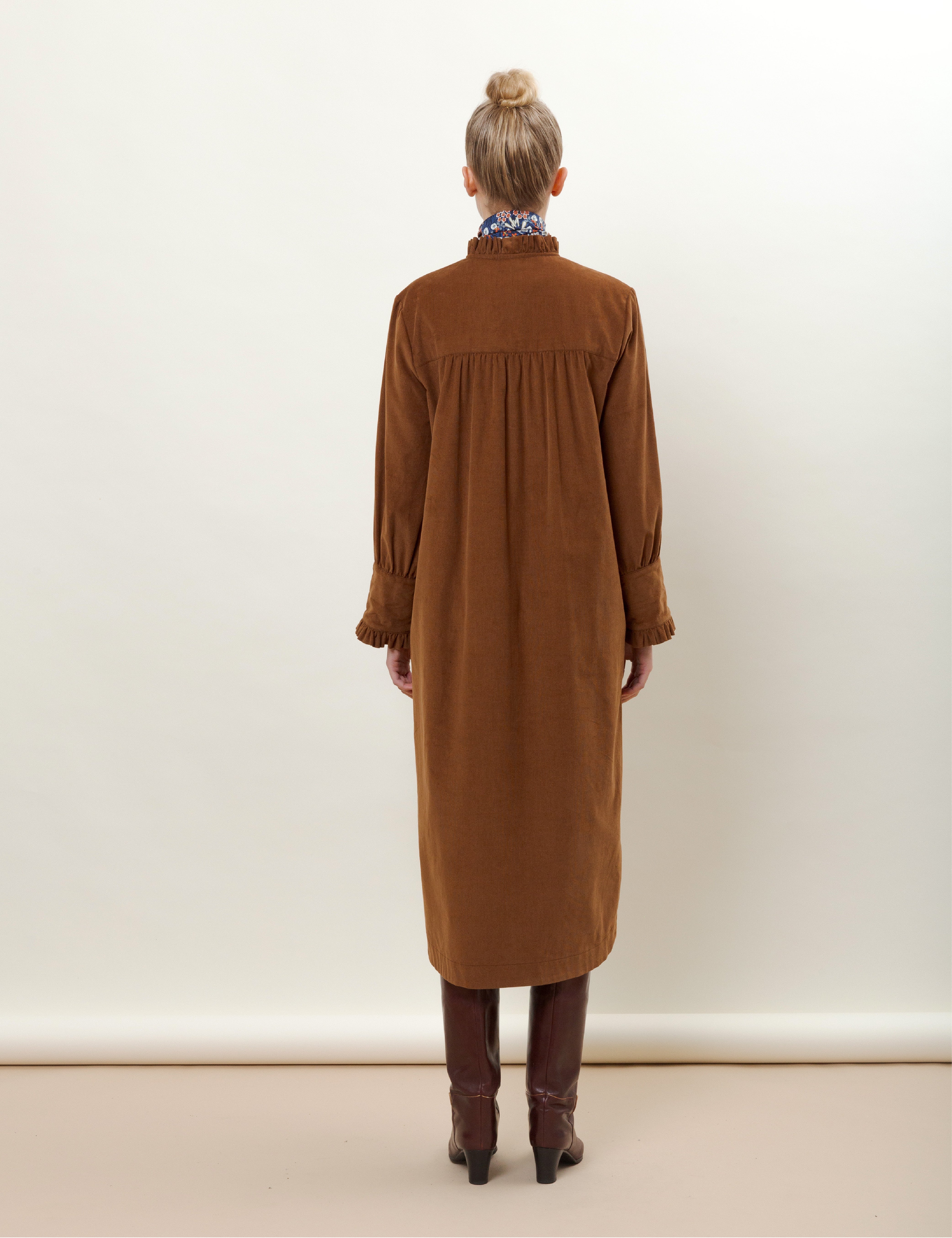 Woman in brown corduroy dress with buttons and frills on the front and flower patterned bandana scarf