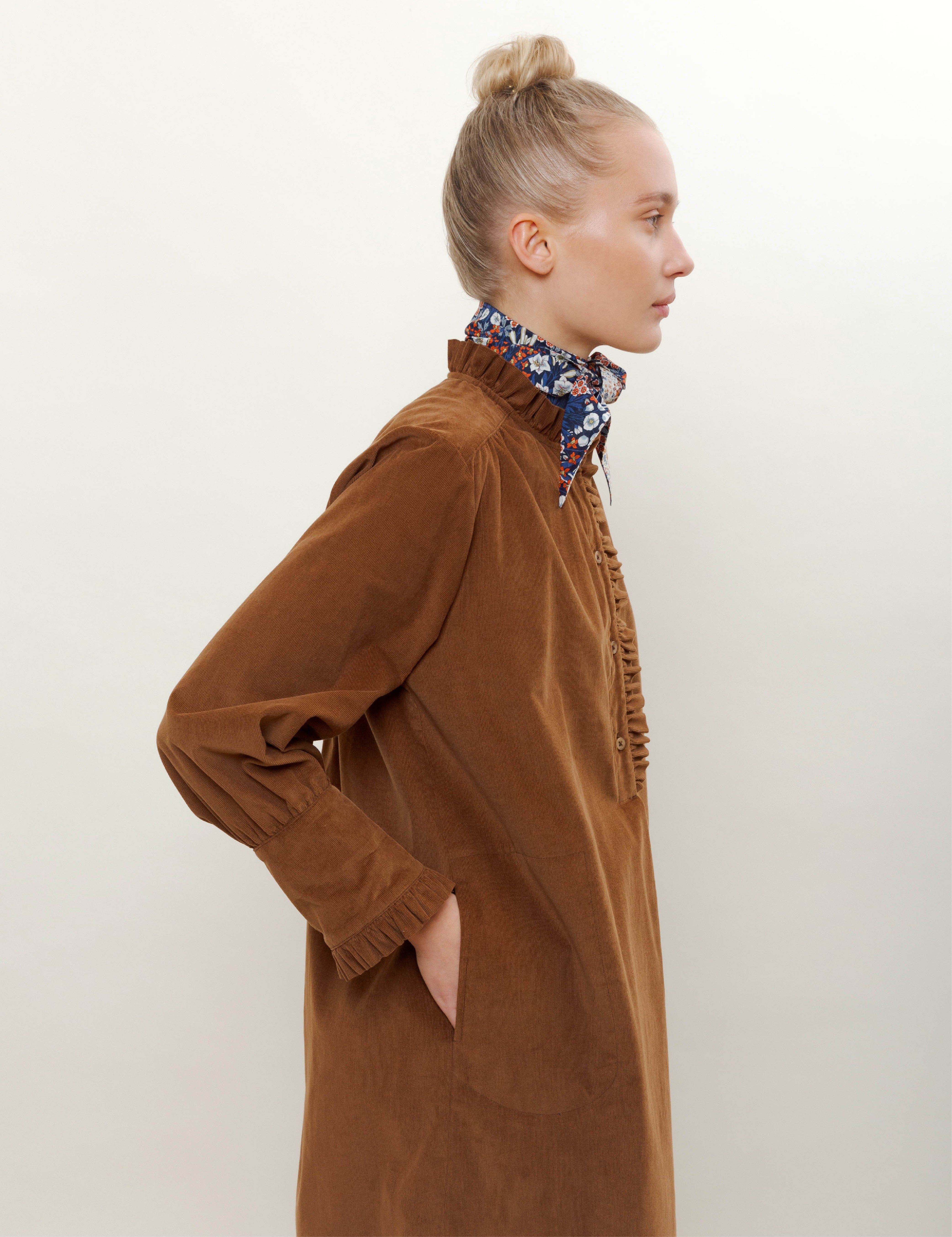 Woman in brown corduroy dress with buttons and frills on the front and flower patterned bandana scarf