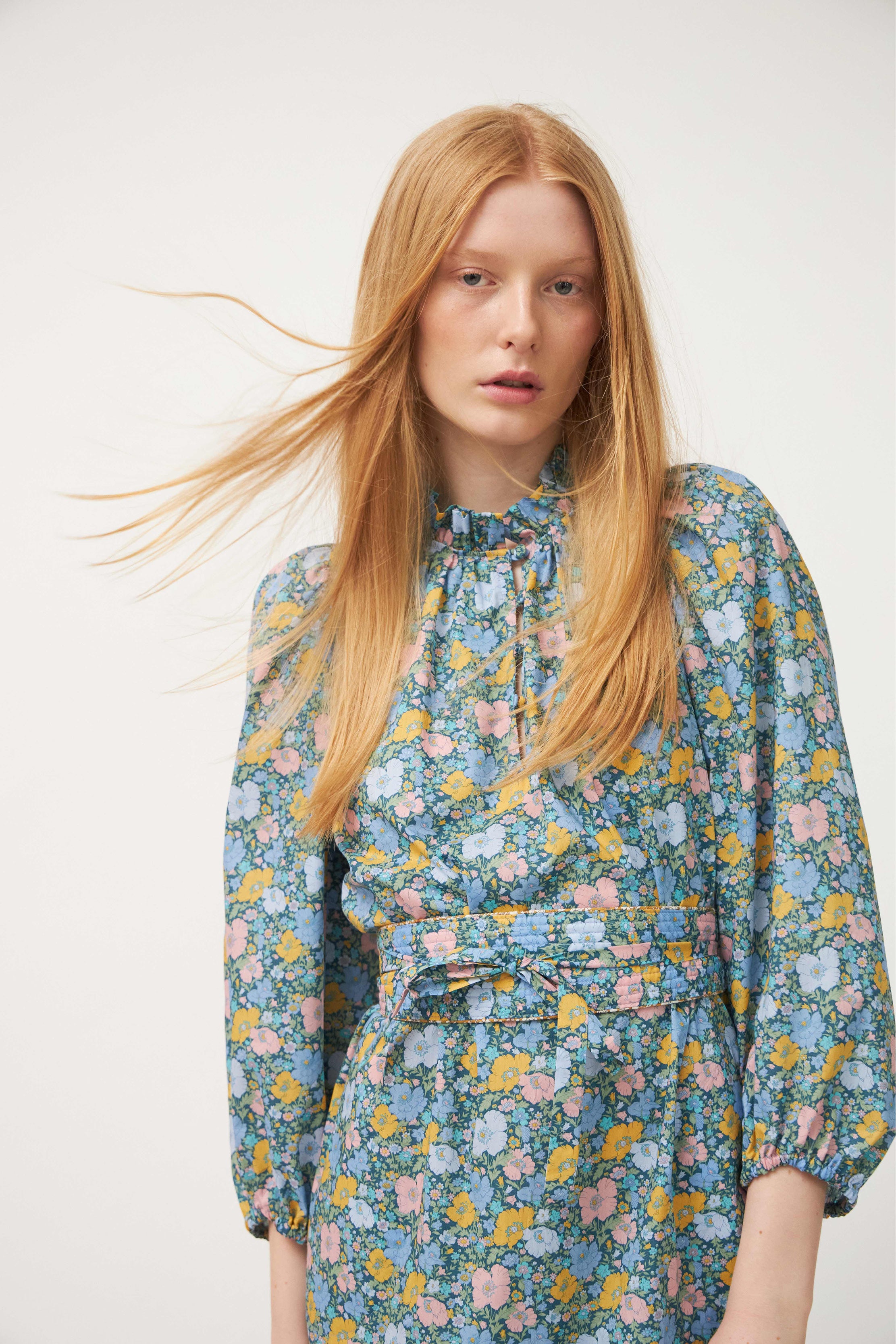 Woman in long dress with multi-colored flower pattern, puffed long sleeves and belt