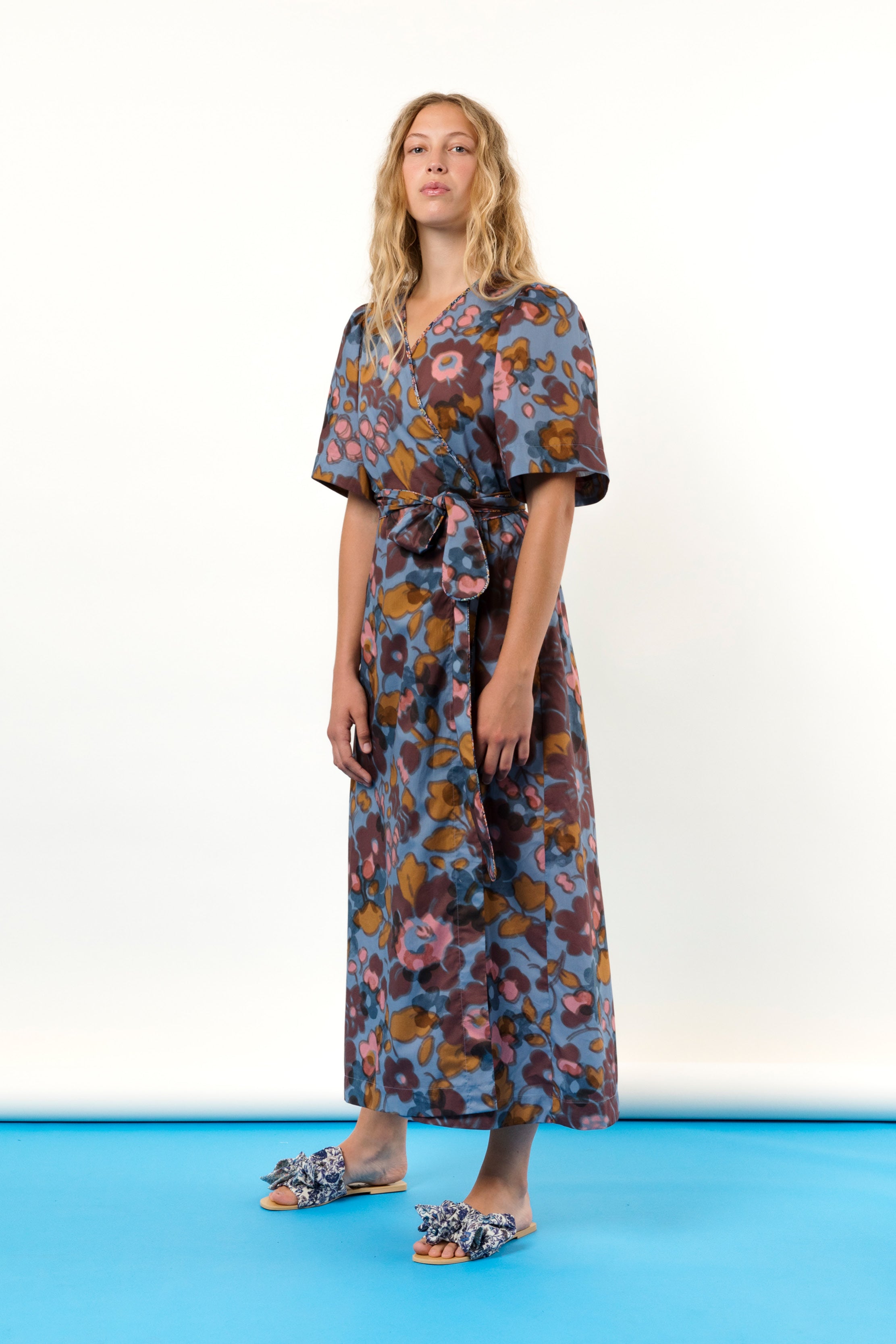 Woman in blue pink and burgundy flower patterned wrap dress in Liberty cotton with short sleeves and sandals with bows