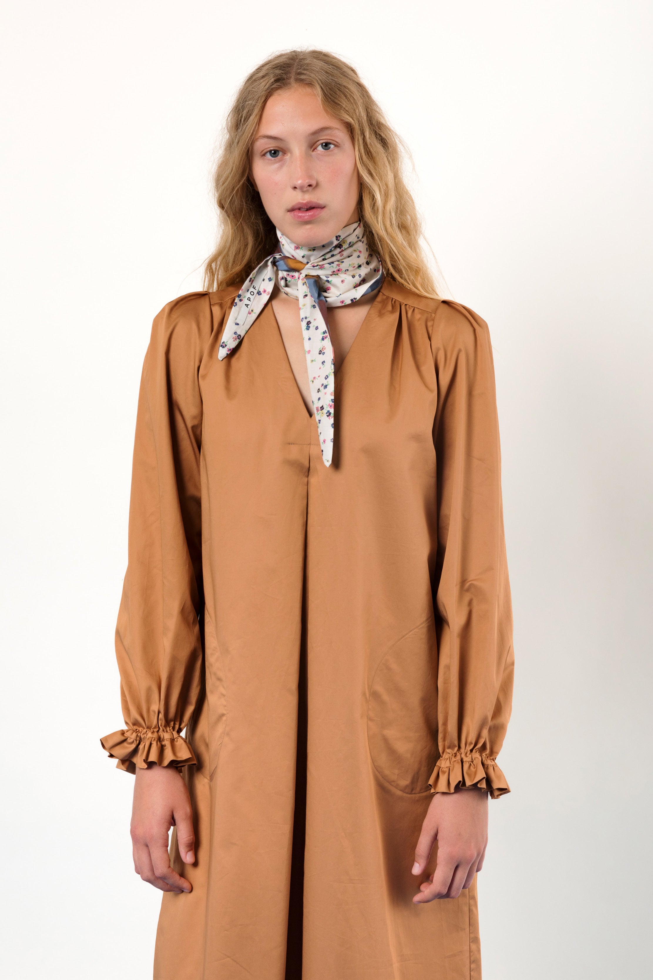 Woman in long brown cotton tunic dress with v-neck, puffed long sleeves, frilled cuffs and bandana around neck