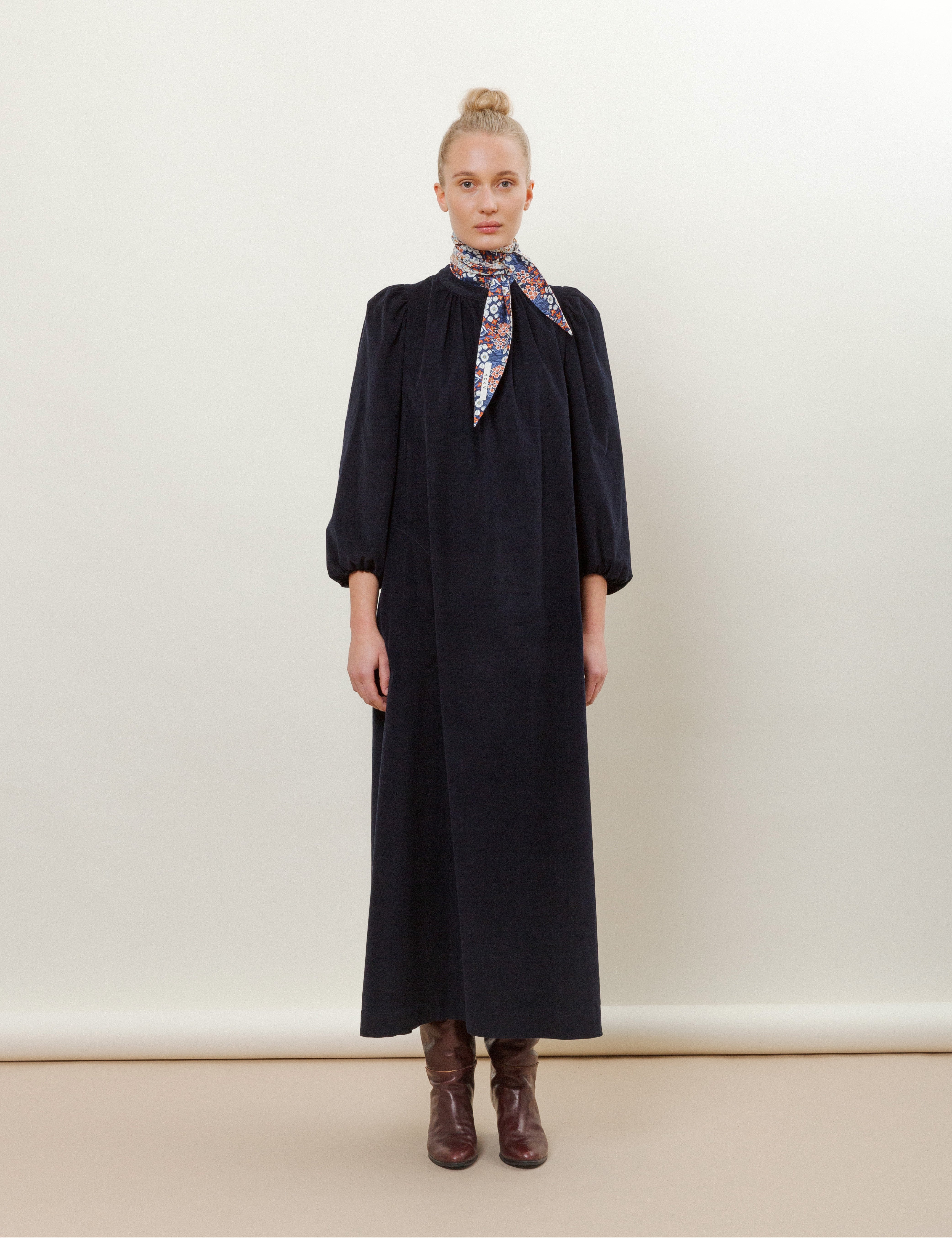 Woman in long navy blue corduroy dress with flower patterned scarf and brown boots