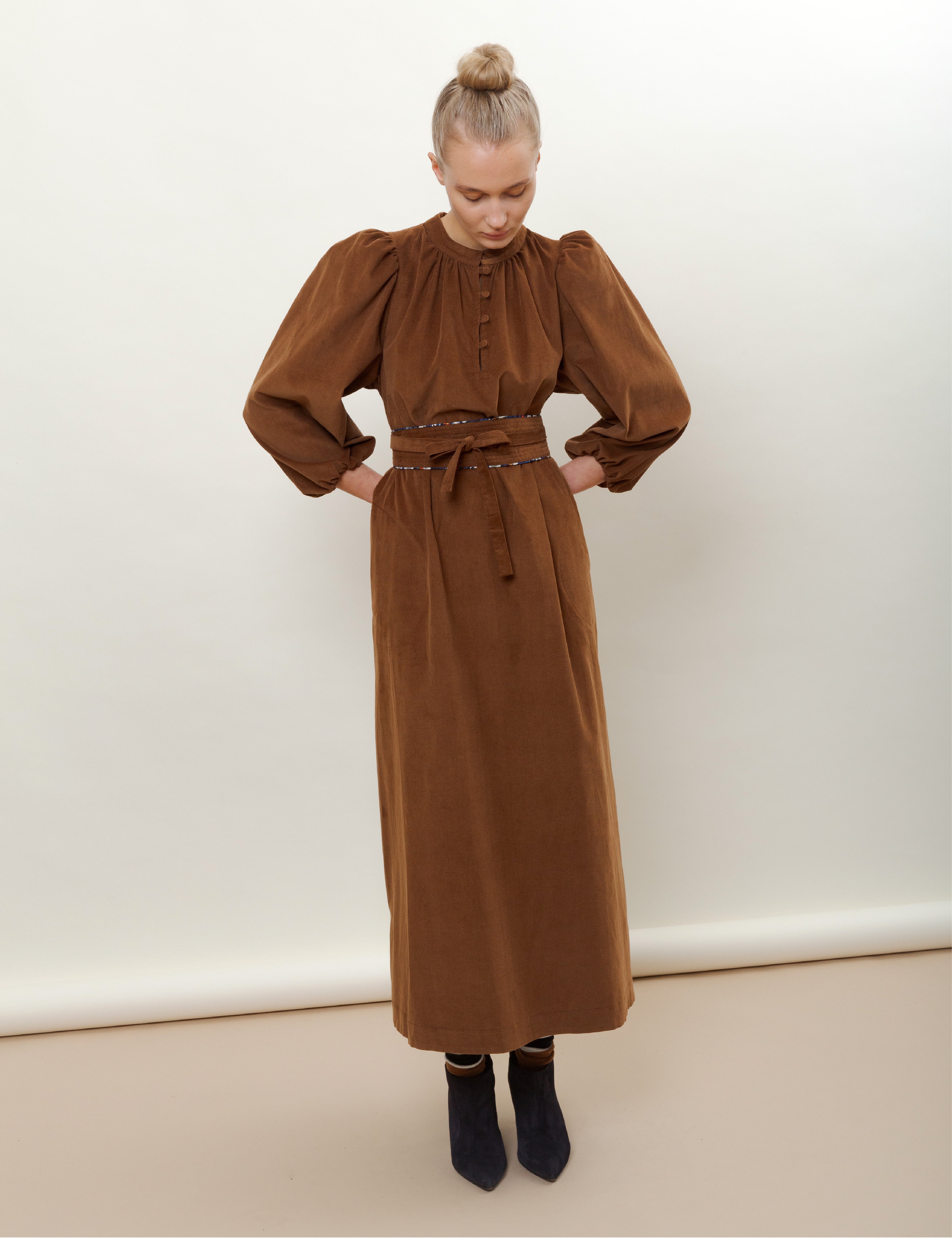 Woman in long brown corduroy dress with belt and black boots