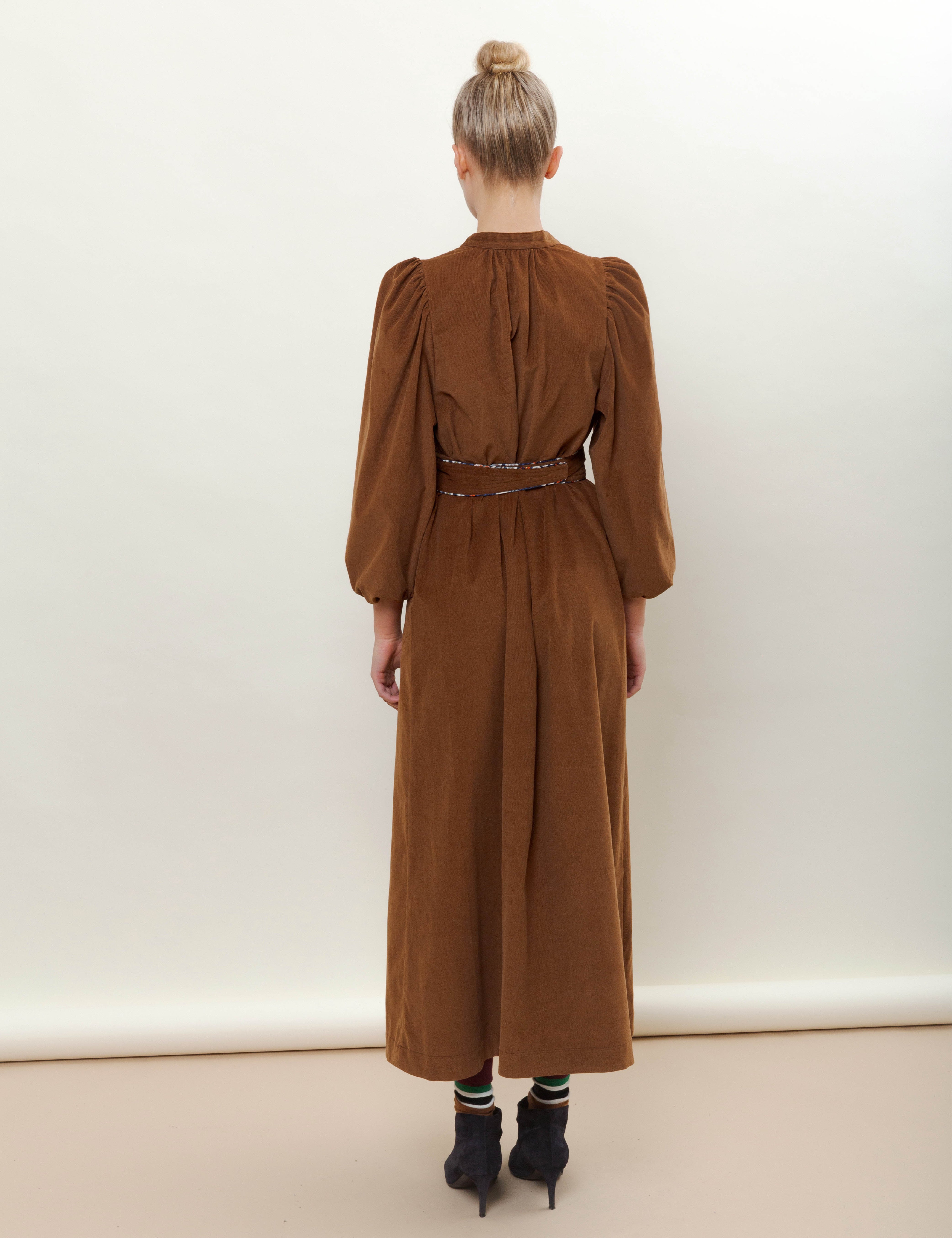 Woman in long brown corduroy dress with belt and black boots