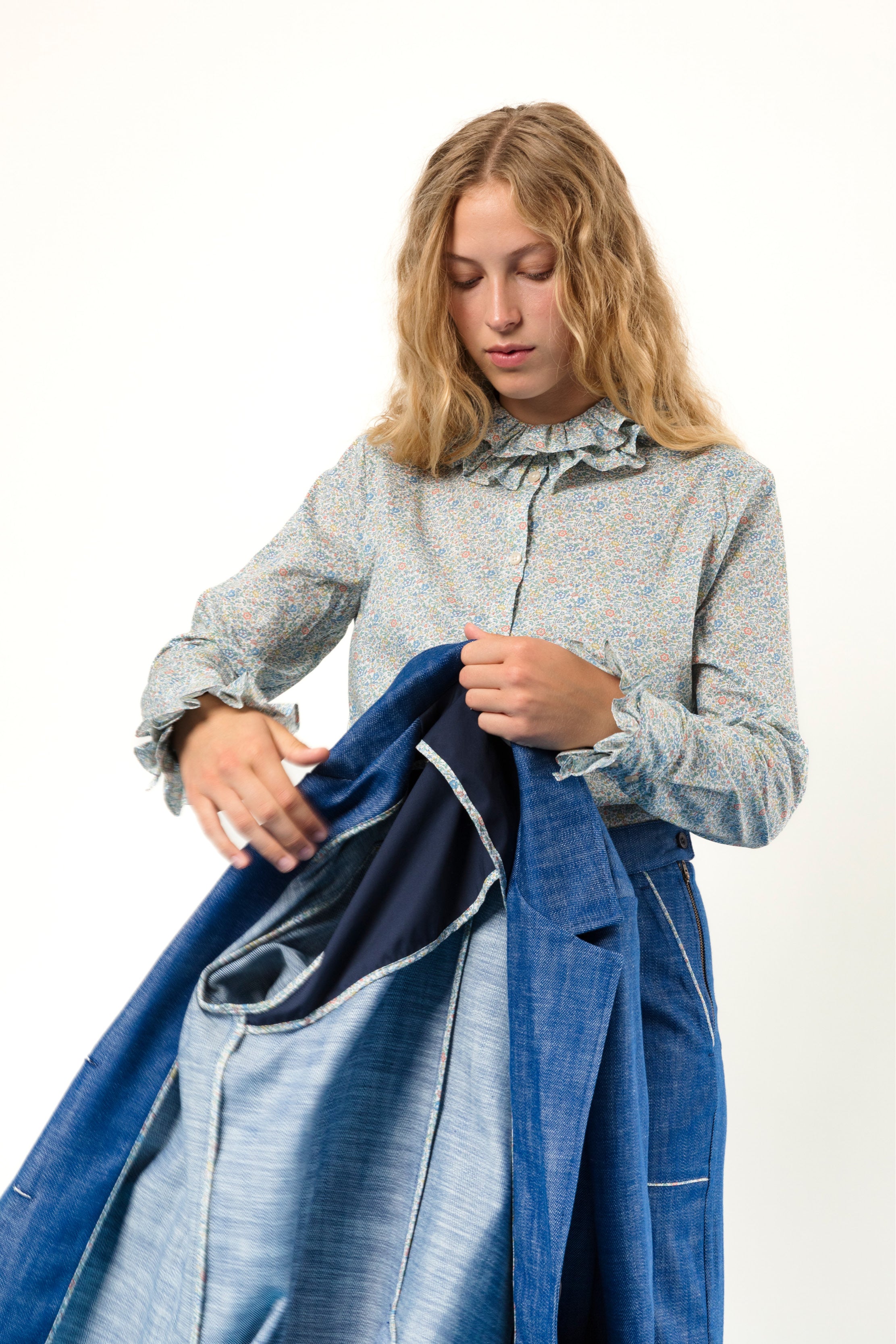 Woman in long sleeved green blouse with flowers and frills holding blue jacket