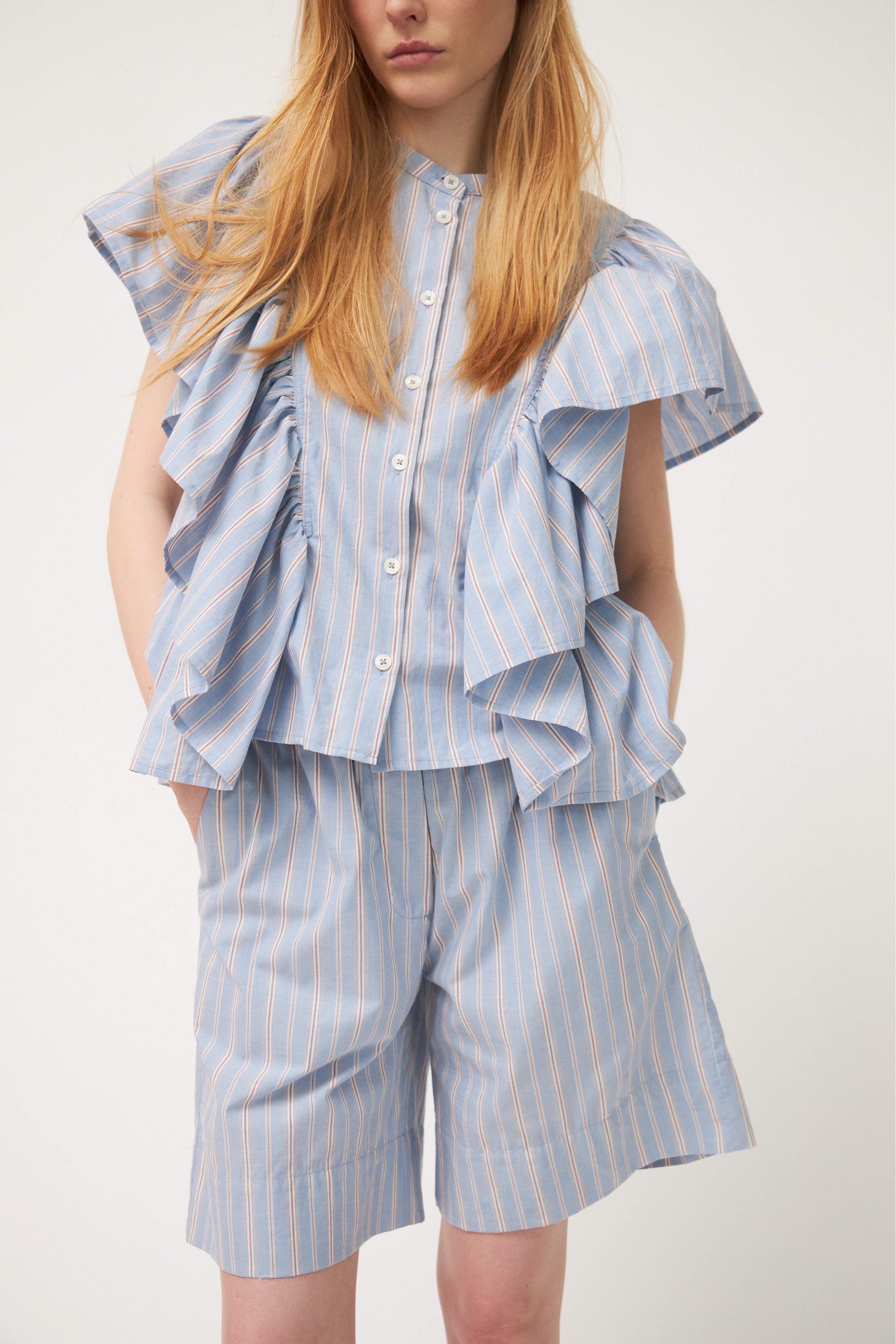 Woman in cotton shorts with blue, red and white stripes and striped blouse with ruffles
