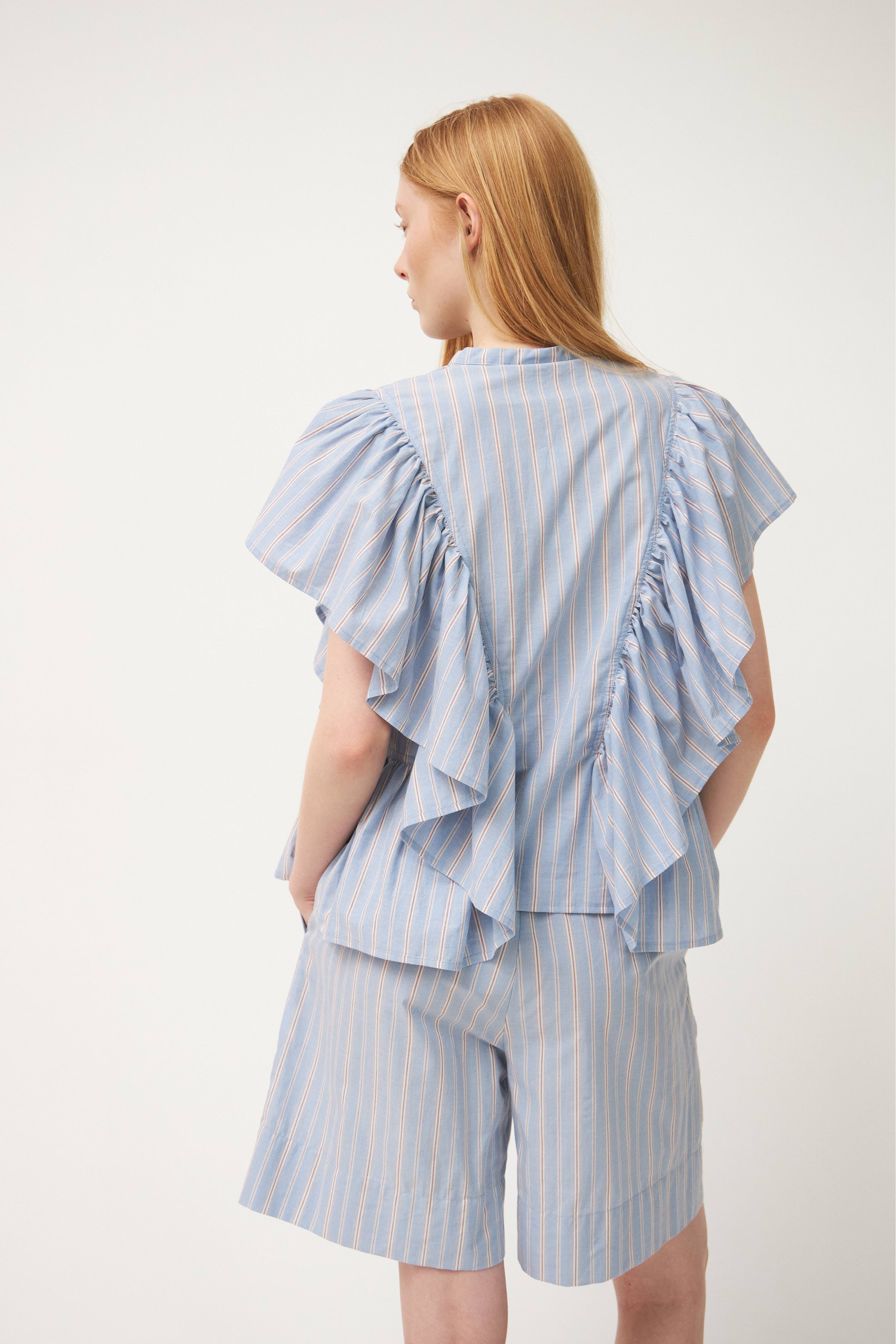 Woman in cotton shorts with blue, red and white stripes and striped blouse with ruffles