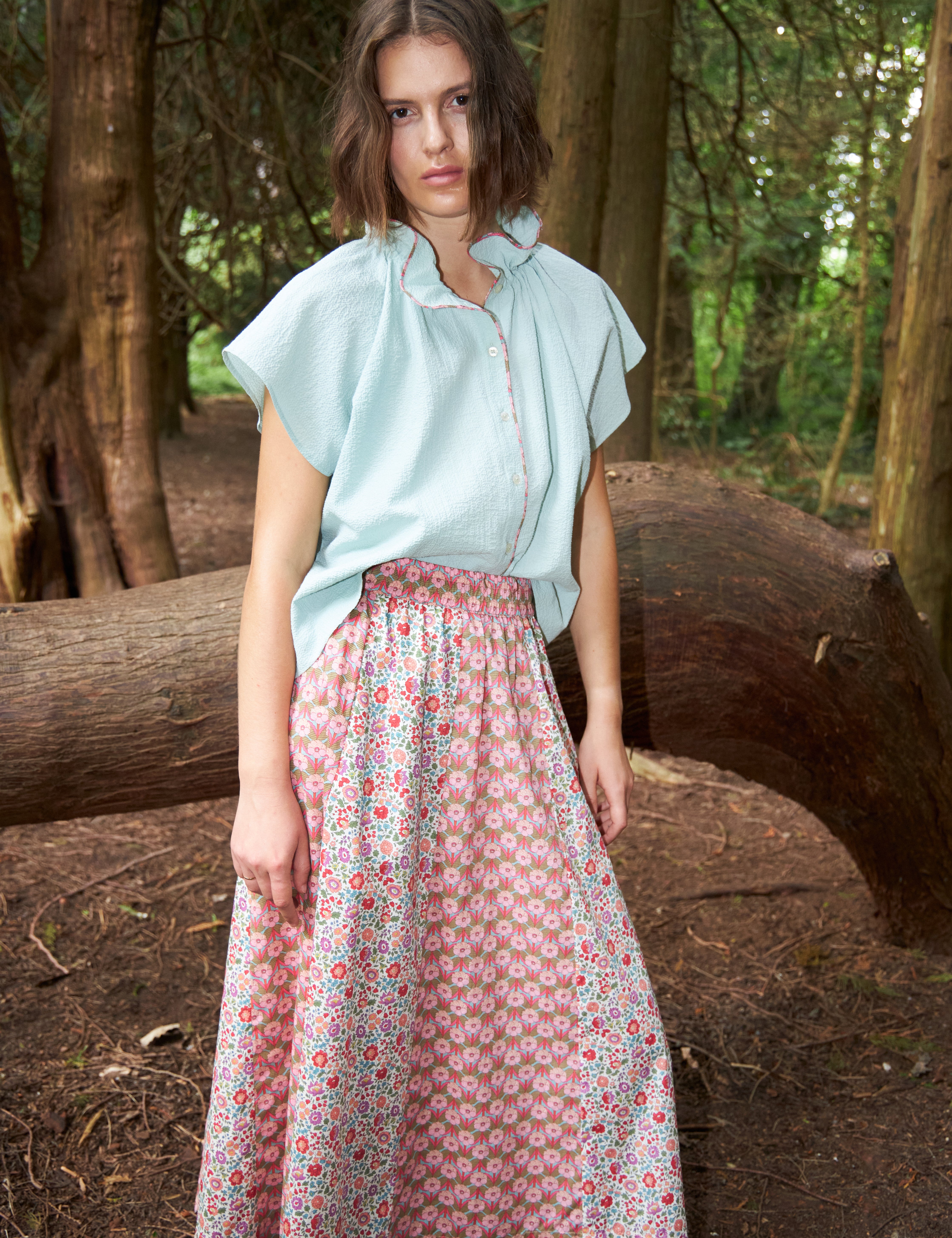Woman in maxi skirt with two different floral prints in pink red and green and blue sleeveless top with frilled stand collar