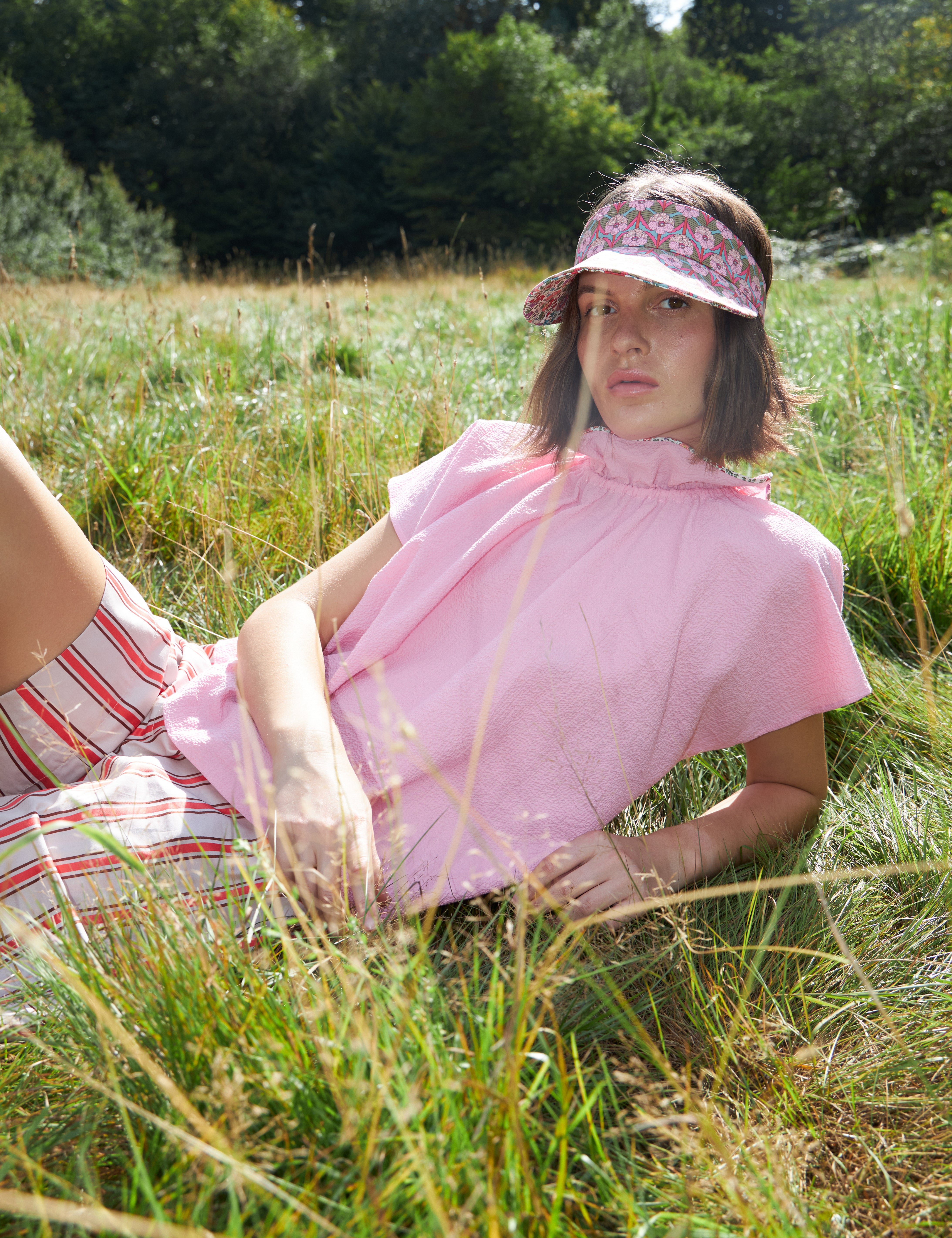 Woman in pink sleeveless top with stand collar and red and white striped shorts and flower print sun cap