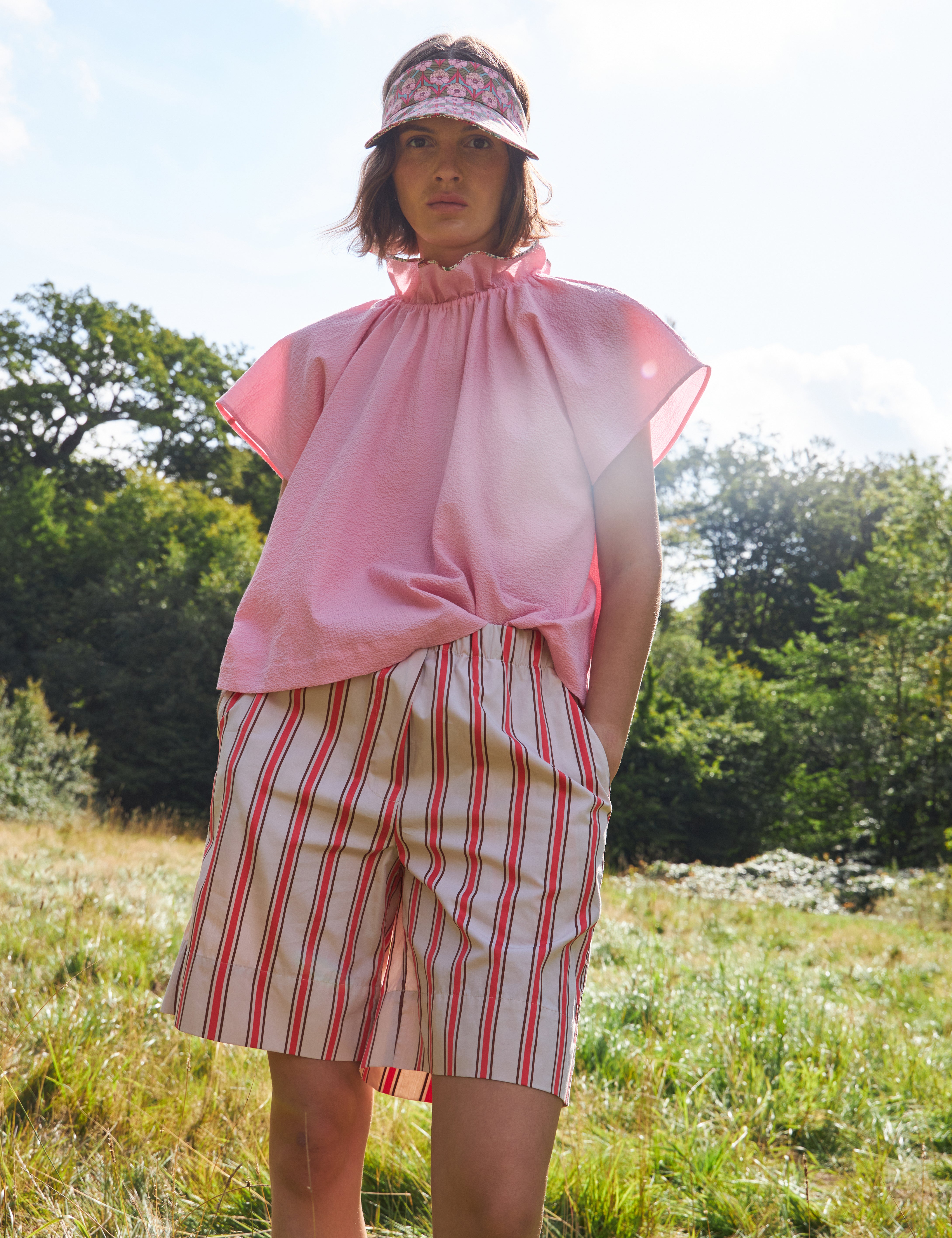 Woman in pink sleeveless top with stand collar and red and white striped shorts